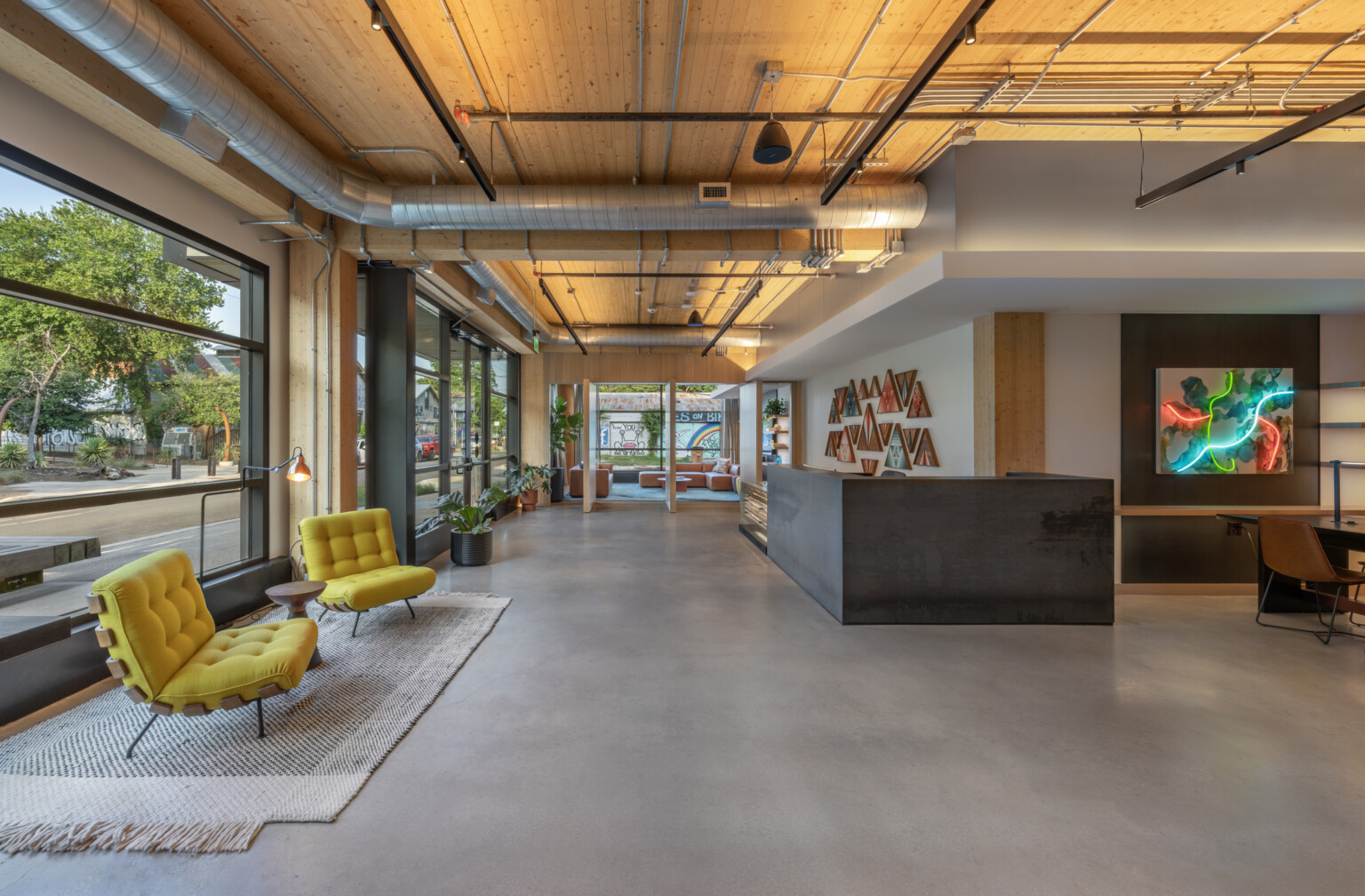 Modern office lobby with large floor to ceiling windows, yellow chairs on a natural rug, modern artwork with neon lighting