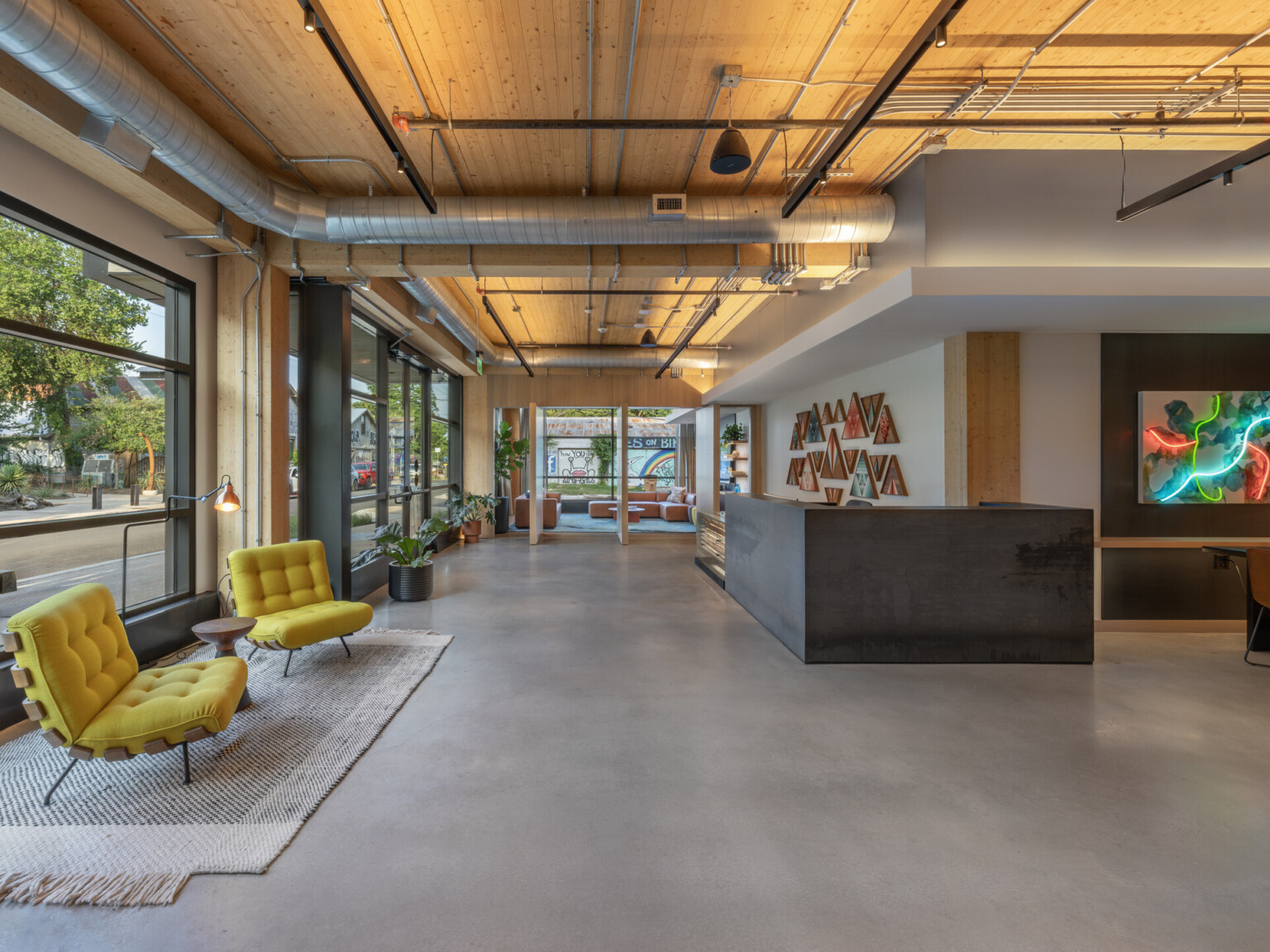 Modern office lobby with large floor to ceiling windows, yellow chairs on a natural rug, modern artwork with neon lighting