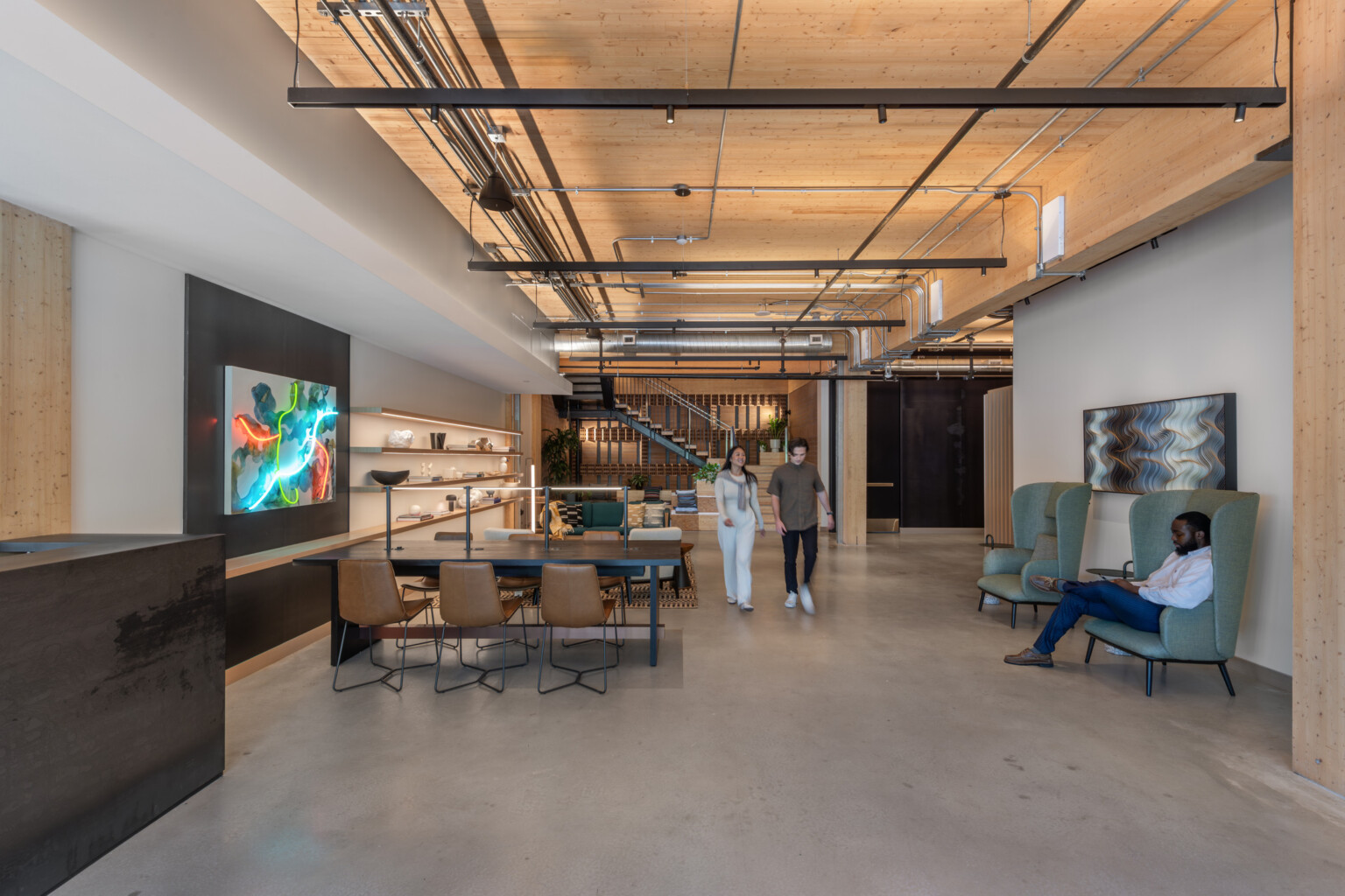 Office collaboration space with wooden ceiling, exposed pipes, multiple seating areas and modern artwork on the walls