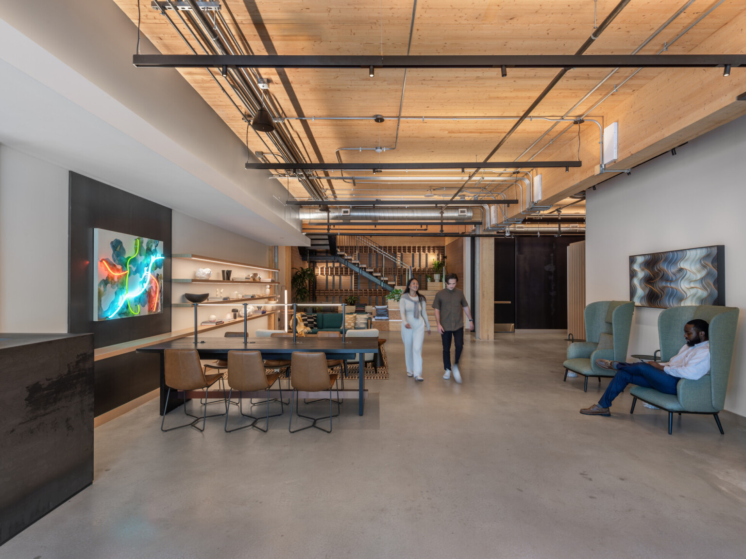 Office collaboration space with wooden ceiling, exposed pipes, multiple seating areas and modern artwork on the walls