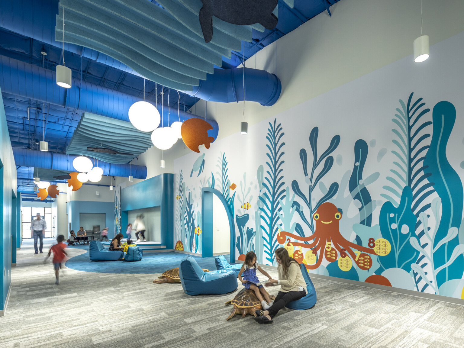 excellence early learning center with colorful ocean murals in blues and orange on the back wall. Light wood flooring and modern furniture.