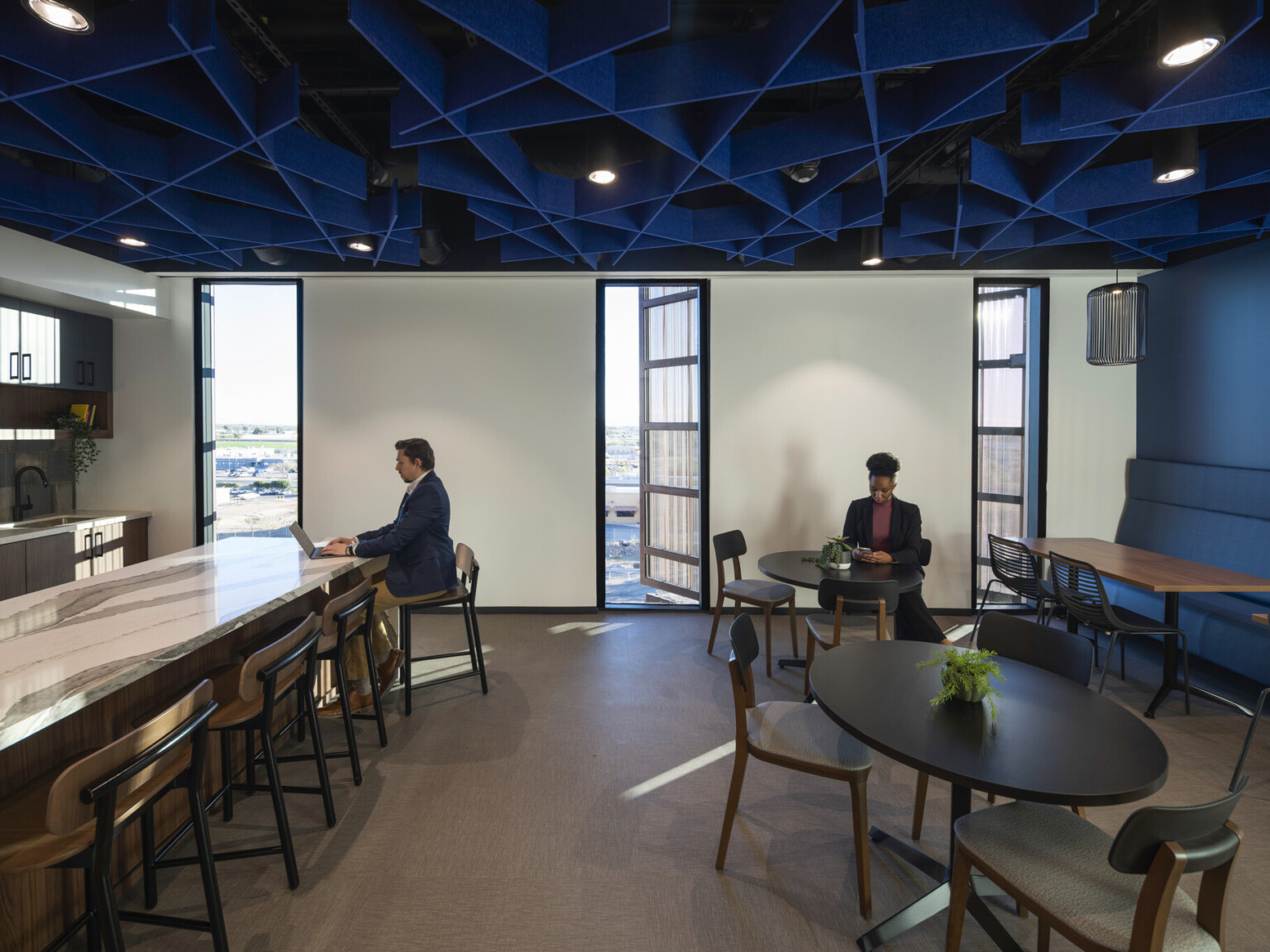 Office common space with blue accent wall and textural ceiling over mixed seating and marble counter, kitchenette left