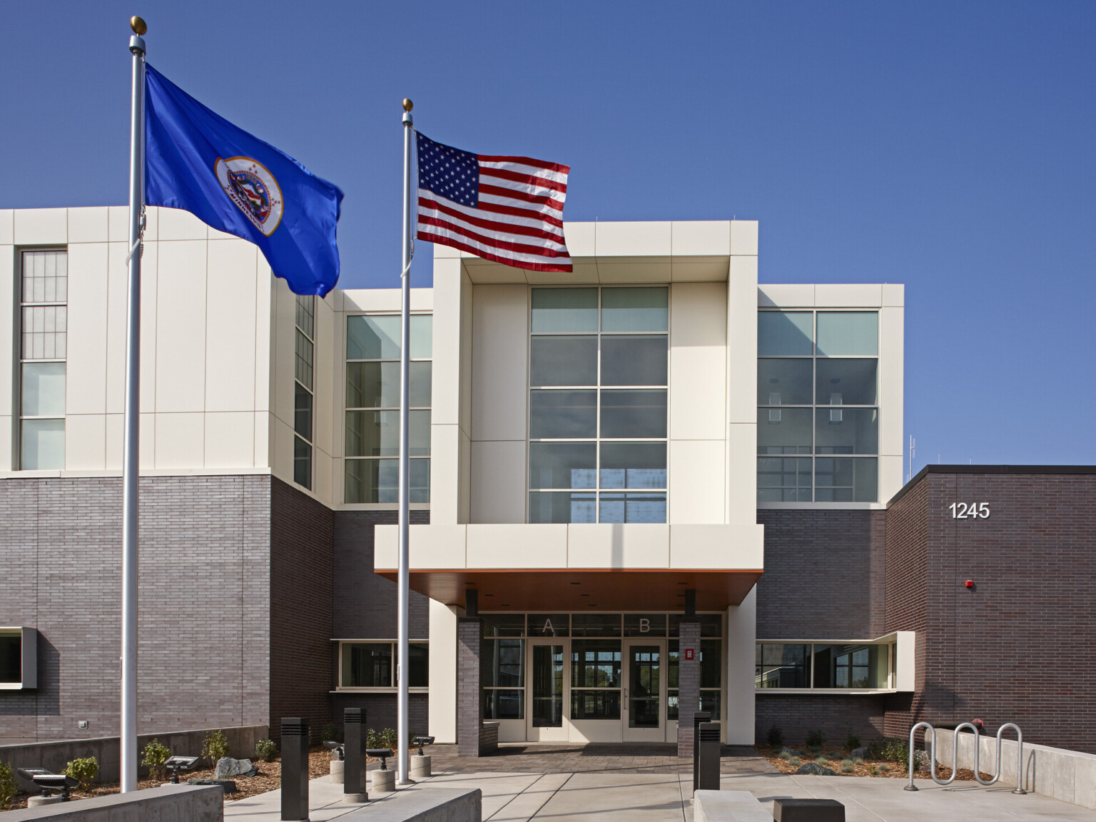 Entry way of a multistory building with a dark brown bottom and white top with an American flag and a blue flag flying out front