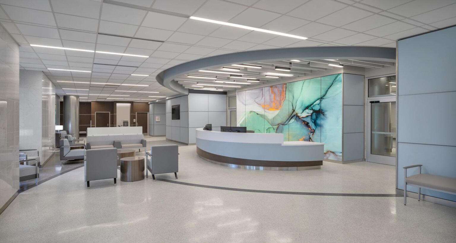 Hospital waiting room with grey and white floors, dark brown accent wall, with a modern geode mural on the wall behind a desk.