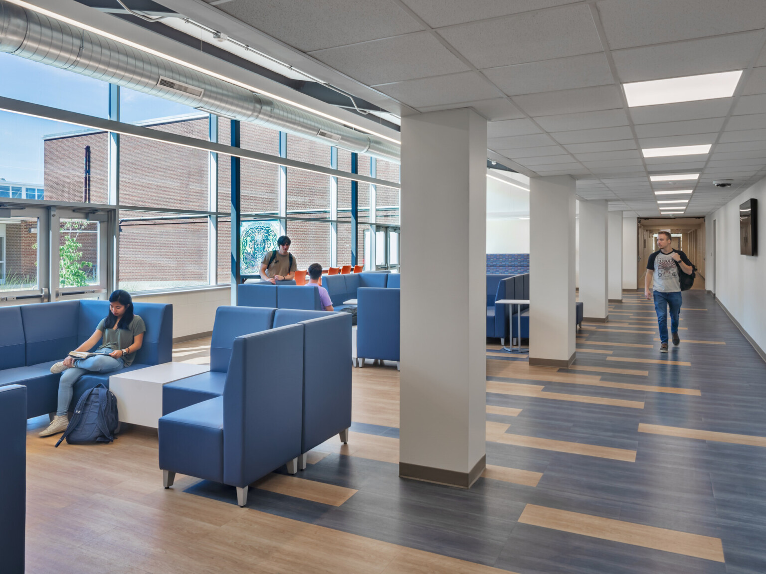 Open concept collaboration area with blue and natural wood floors, blue high-back seating areas, and large glass windows