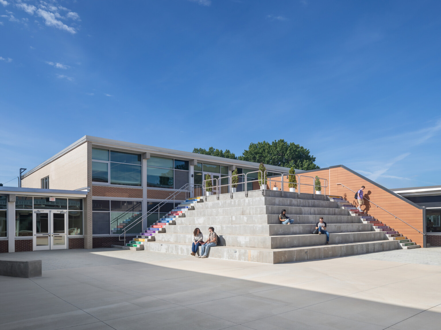 Outdoor courtyard in from of a two story building with large stairs leading up to the second story providing seating areas for students