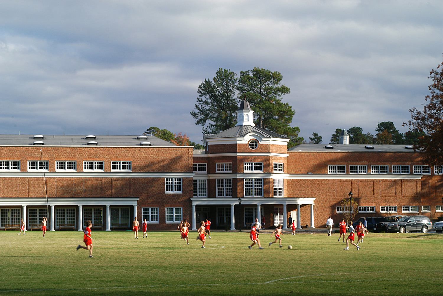 Multistory brick building with white accents behind a soccer field filled with kids playing