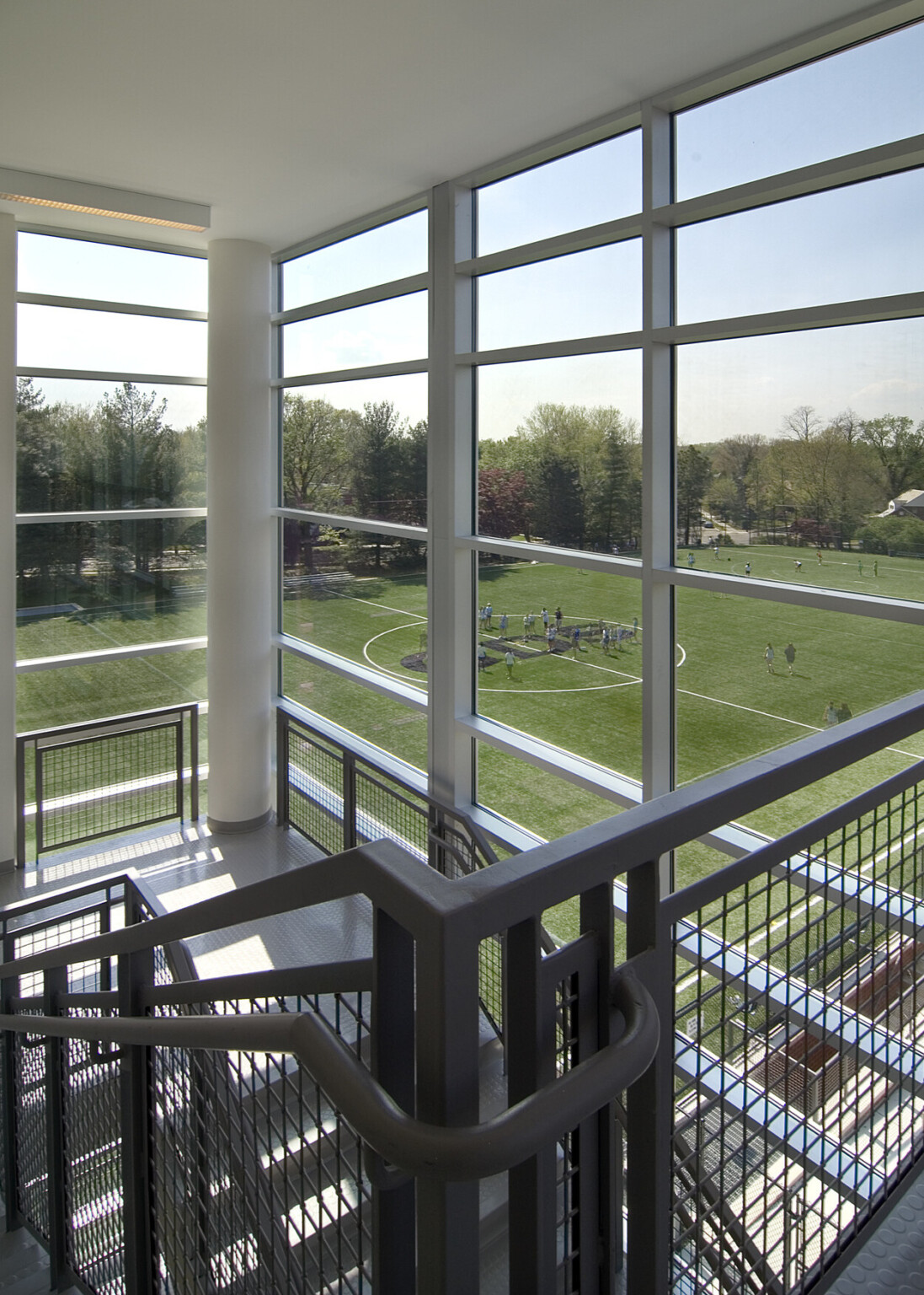 Stairway surrounded by floor to ceiling windows overlooking a lush green playing field