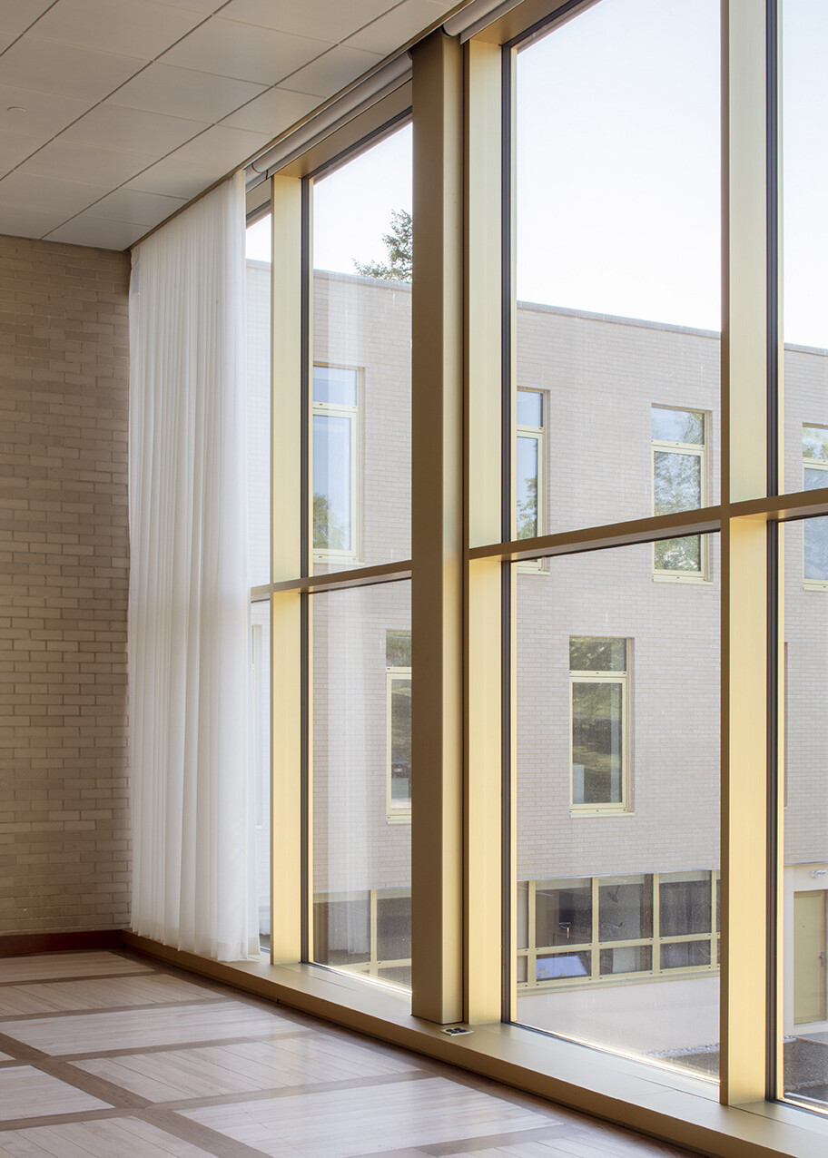 Floor to ceiling picture frame windows line hallway, shadow of panes from abundance of natural light in the workplace