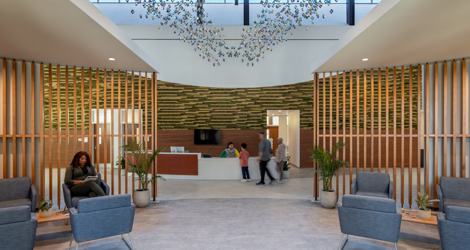 Medical office waiting room with modern fixture suspended from ceiling, wooden accent wall dividing seating area and desk area