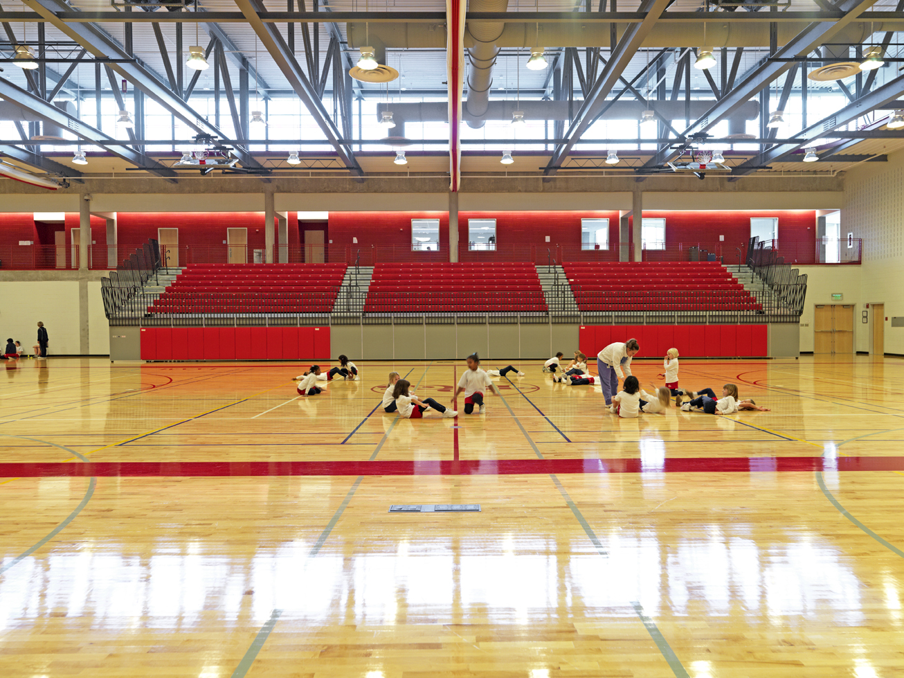 A basketball court with vibrant red and natural wood flooring, complete with hoops and boundary lines