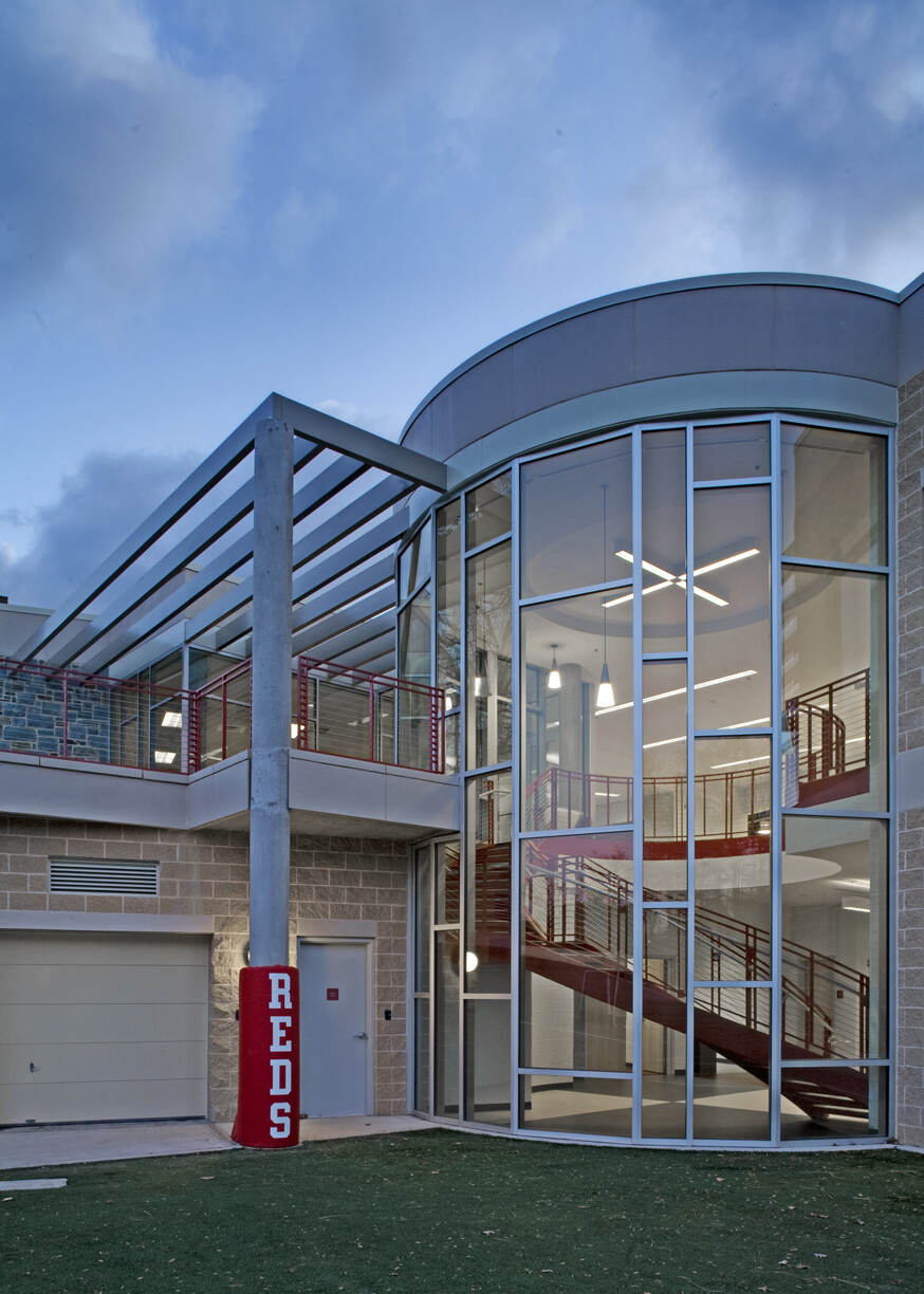 A modern building with staircase behind a rounded glass enclosure with a metal column with a red pad on it that says REDS