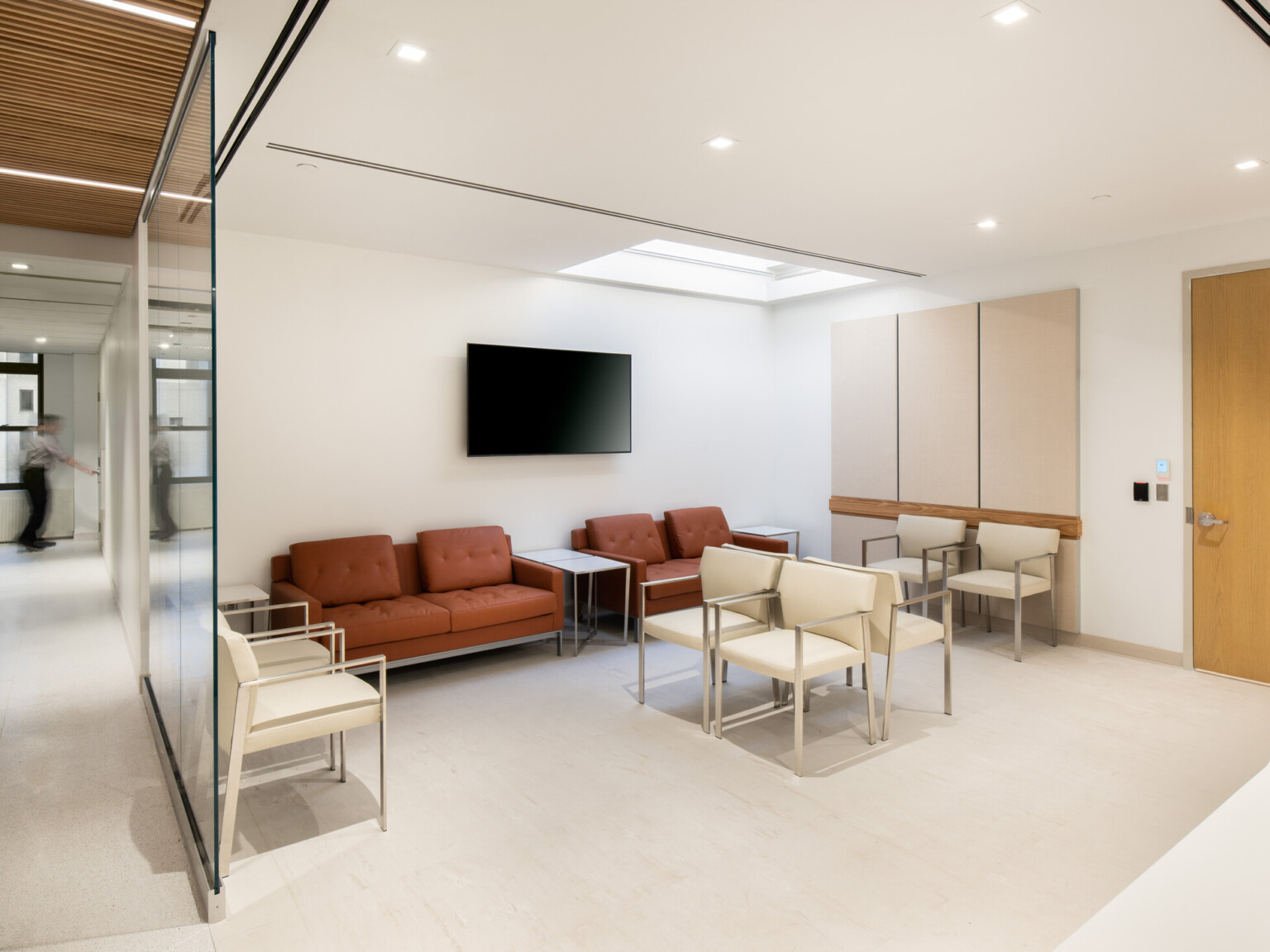 Hospital waiting room filled with modern ivory and terracotta furniture, TV hanging on the backwall and a view down the hallway to the left