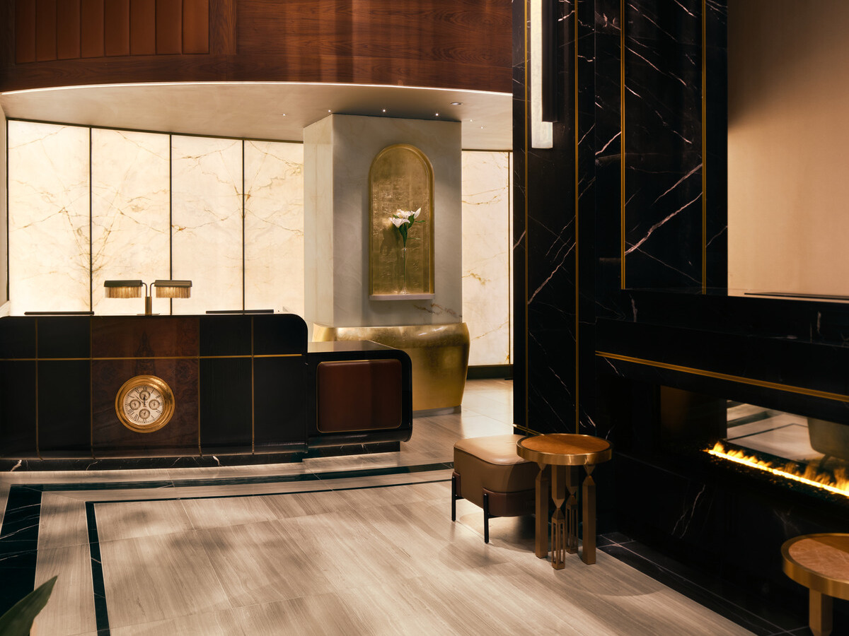 Glamorous hotel lobby showing black marble fireplace with modern furnishings and gold accents suspended from the ceiling