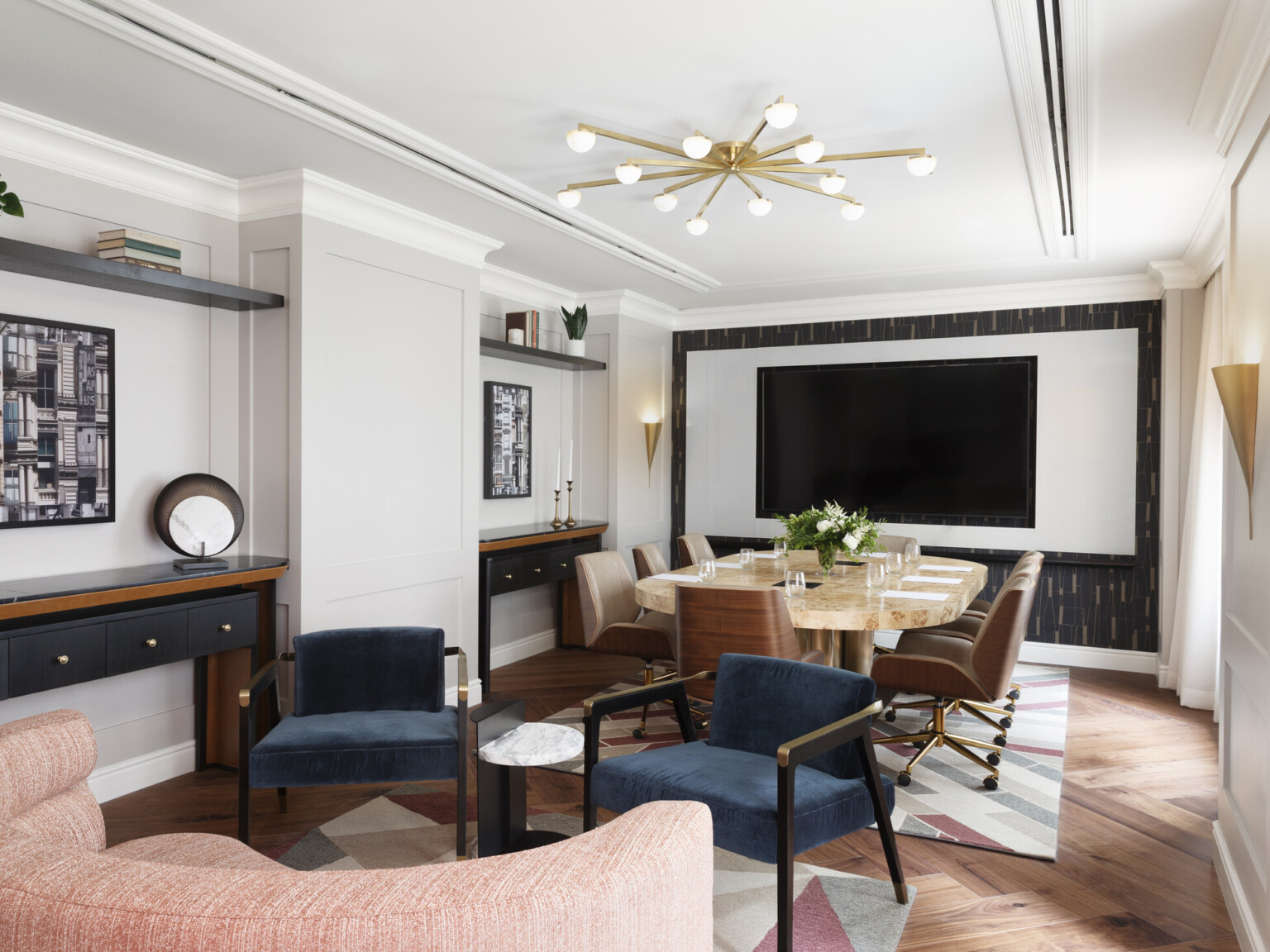 Modern seating area with a table surrounded by chairs in front of a TV hanging on a wall. Modern furnishings and lighting throughout