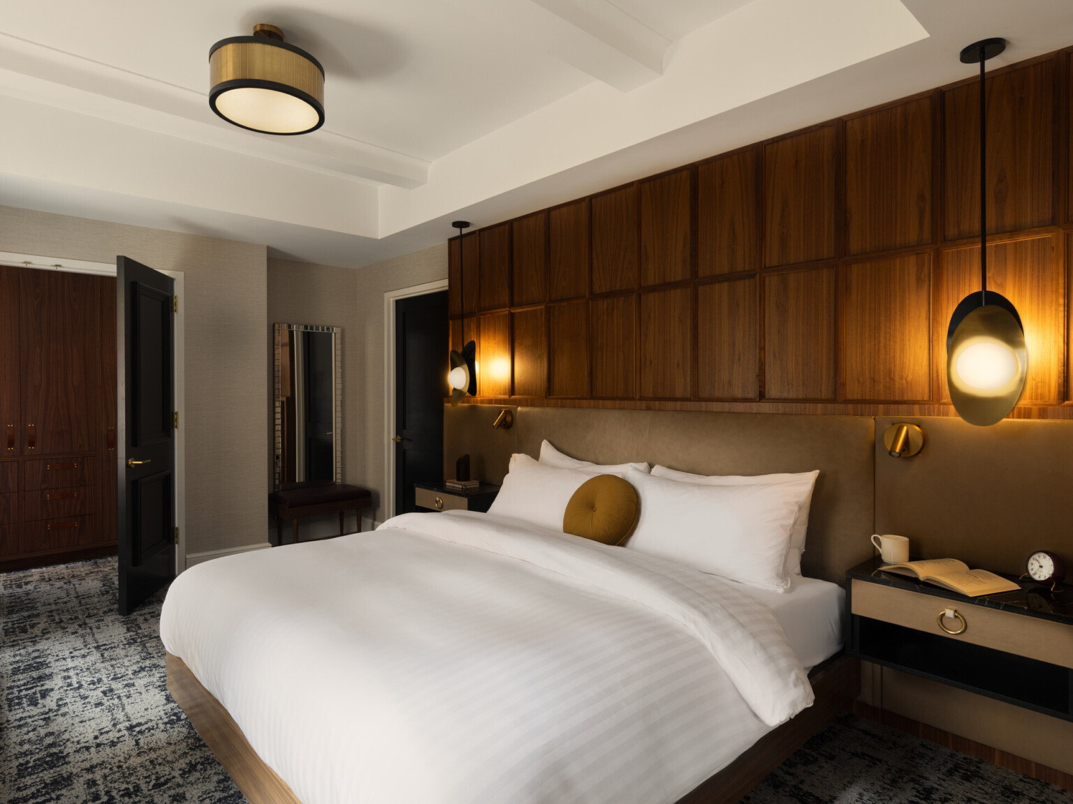 Modern hotel room with black doors, dark grey carpeting, white linens and brown wood accents