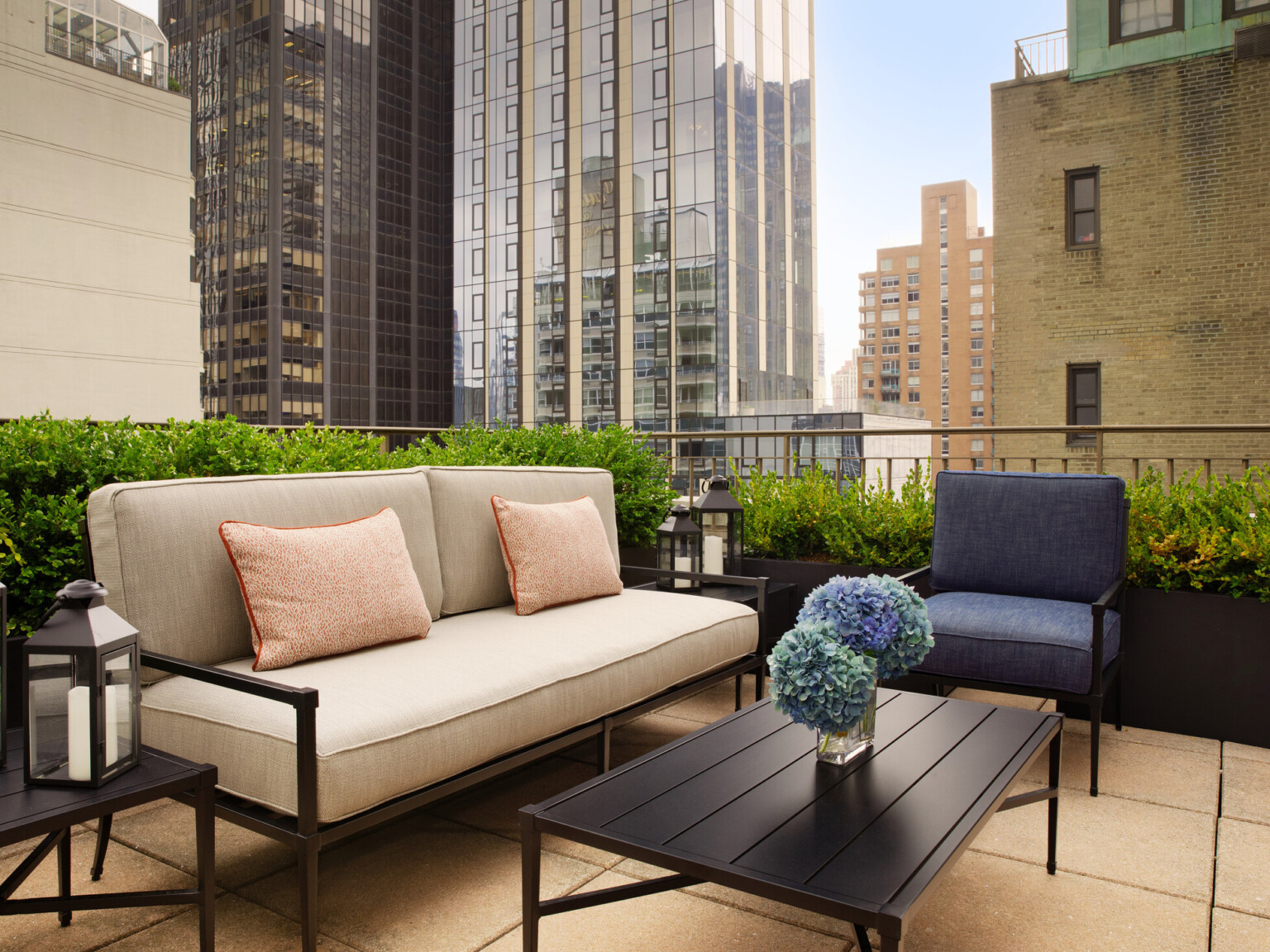 Rooftop seating area with black metal couch and chair with cushions with large skyscrapers in the background