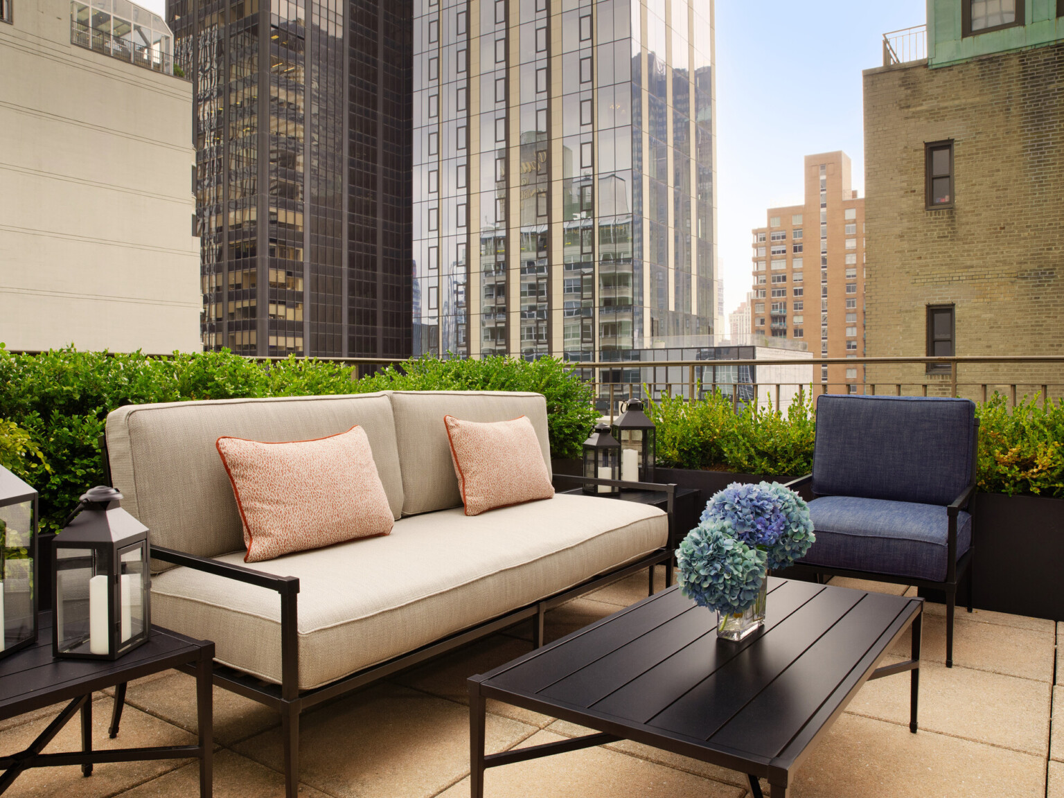 Rooftop seating area with black metal couch and chair with cushions with large skyscrapers in the background