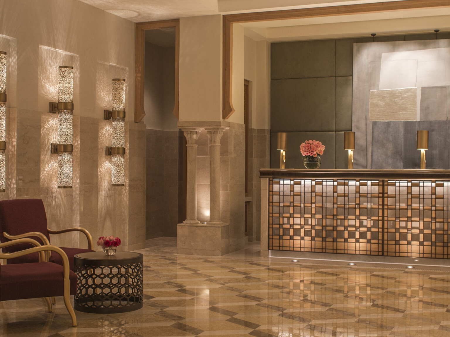 Luxurious hotel lobby with maroon and gold armchairs, ornate decorative lights, and reception desk with gold accents.