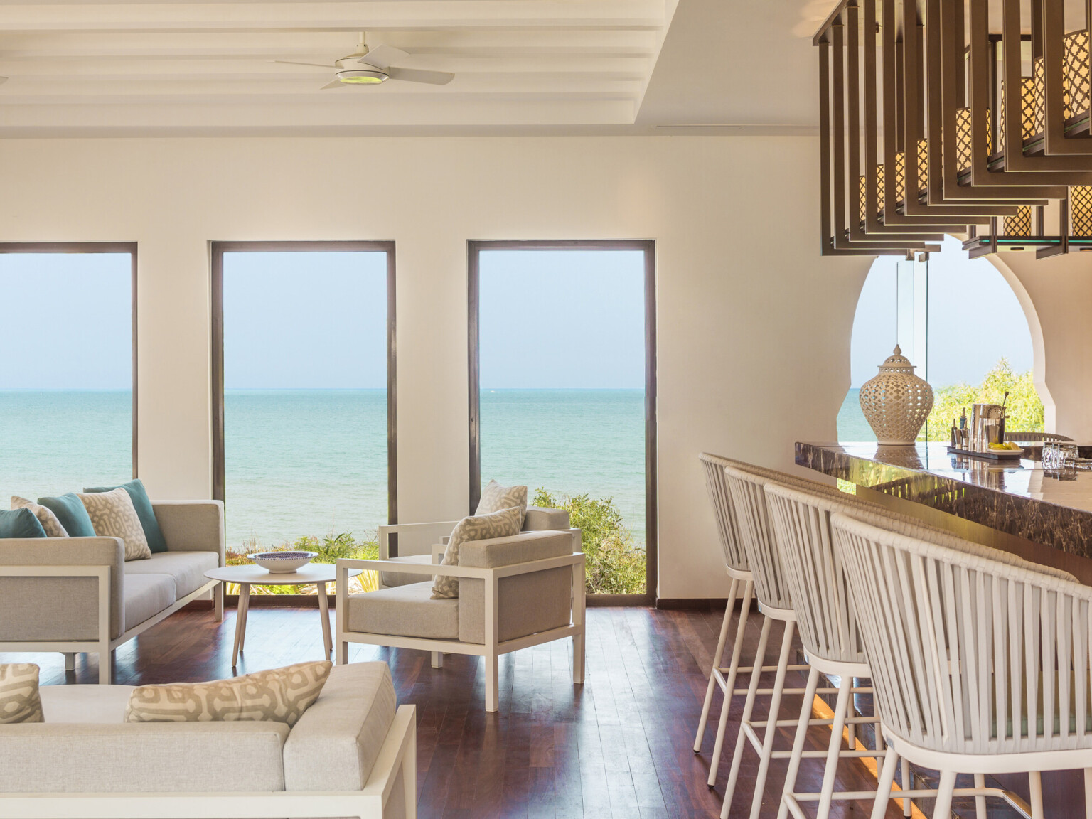 Stylish lounge with a view of the sea through large windows, featuring white and beige seating, and with white barstools