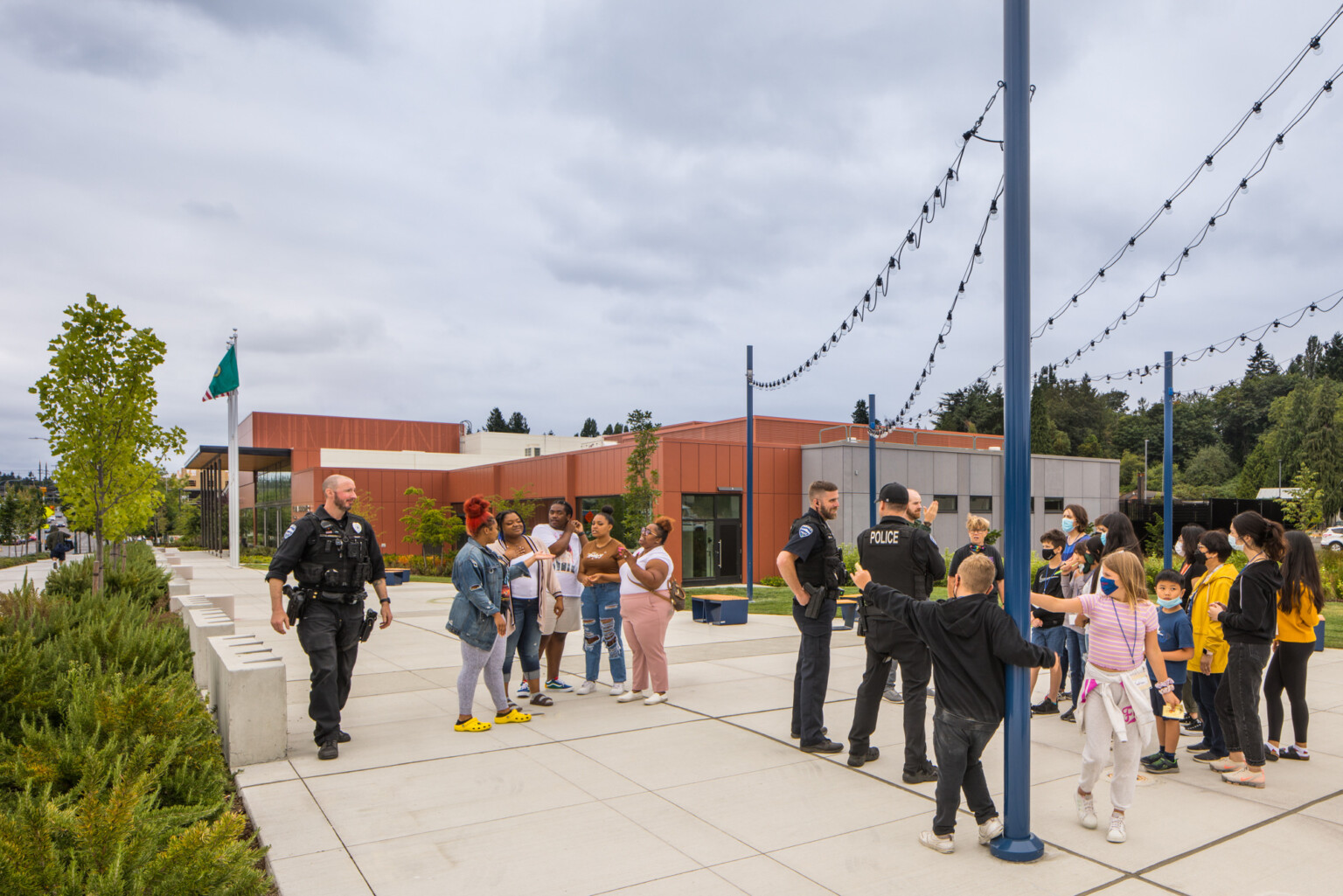 Group of people gathered outside of a orange and grey building with lights strung between blue poles