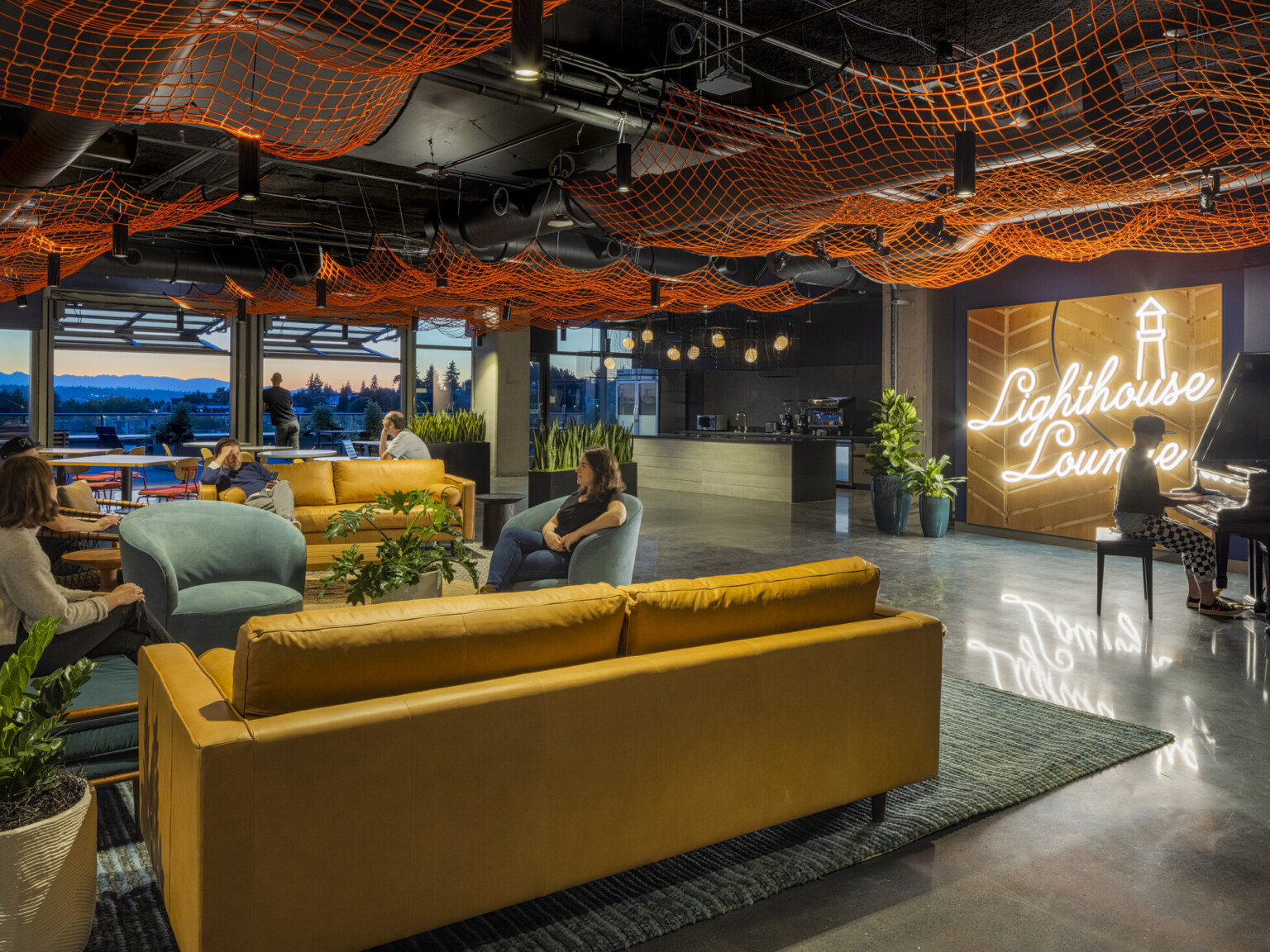 workplace lounge with piano and fishing net art installation, garage doors open to mountain views at sunset