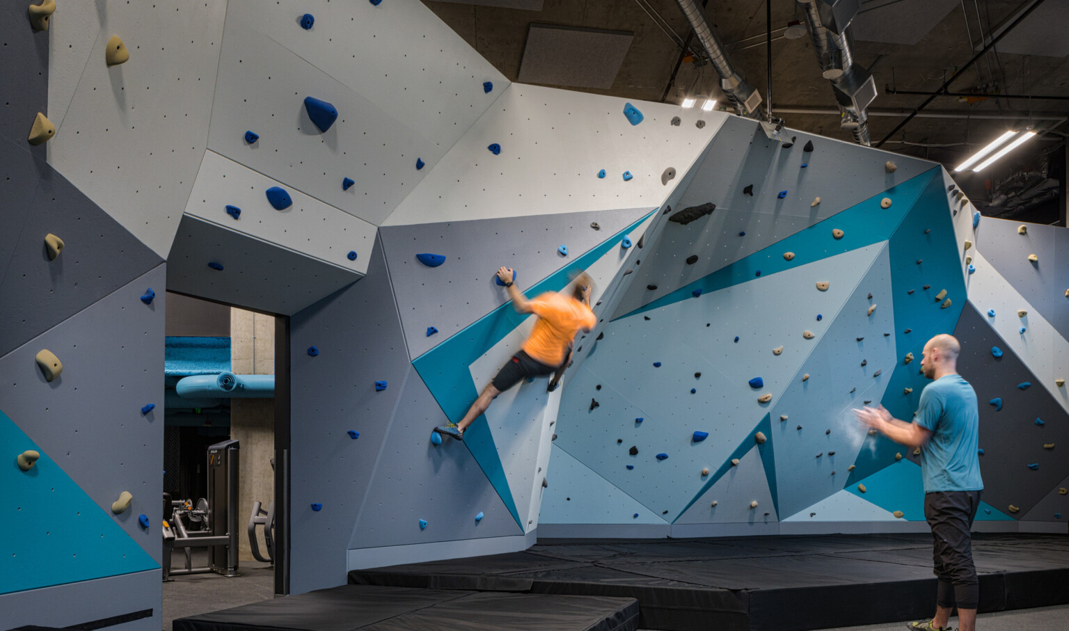 Rock wall in shades of blue with triangular patterns lining the walls. Exposed A/C ducting in the ceiling