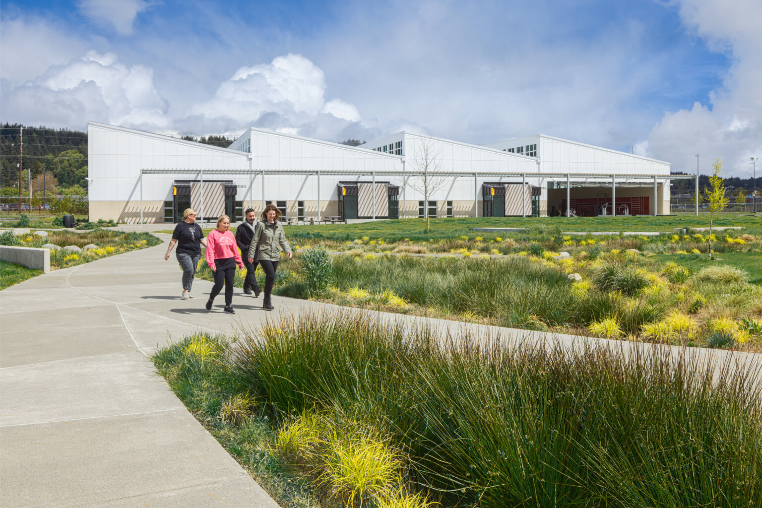 Exterior of the Green Hill school showing a modern white building with angled rooflines, with a covered awning spanning the building. Multiple concrete paths lined with lush landscaping