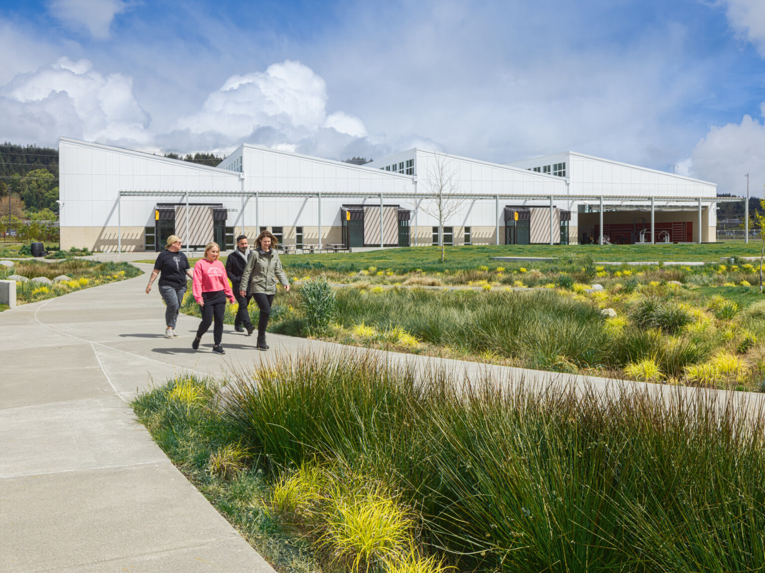 Exterior of the Green Hill school showing a modern white building with angled rooflines, with a covered awning spanning the building. Multiple concrete paths lined with lush landscaping