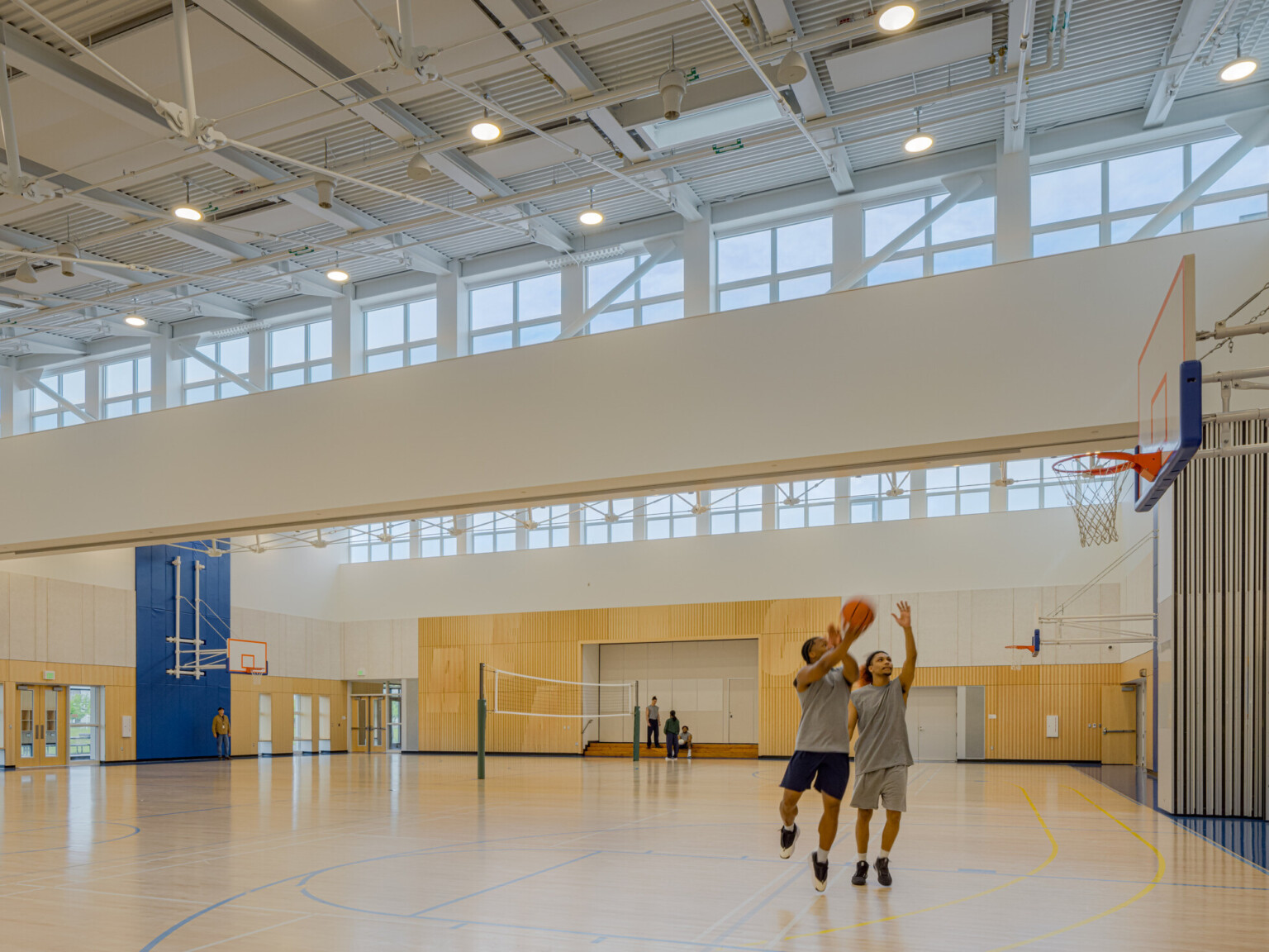 Basketball gym with multiple goals around the exterior and a volleyball net in the middle with two kids in grey shirts playing