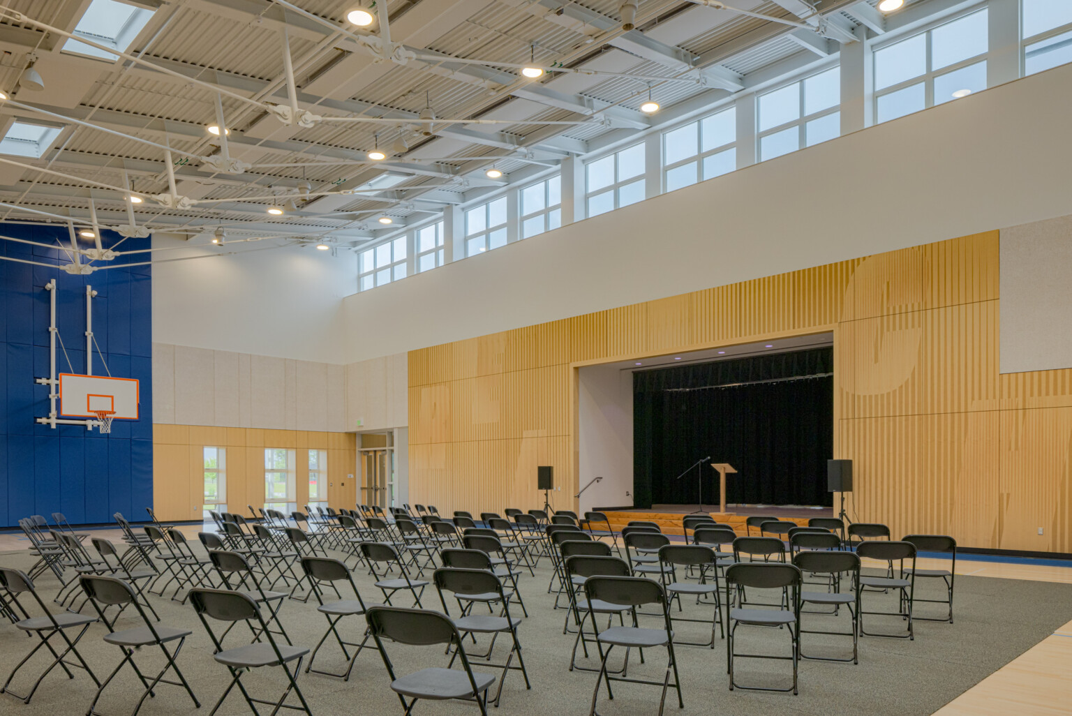 Auditorium with wall lined with wood with a cutout for a stage with a podium and microphone in the middle