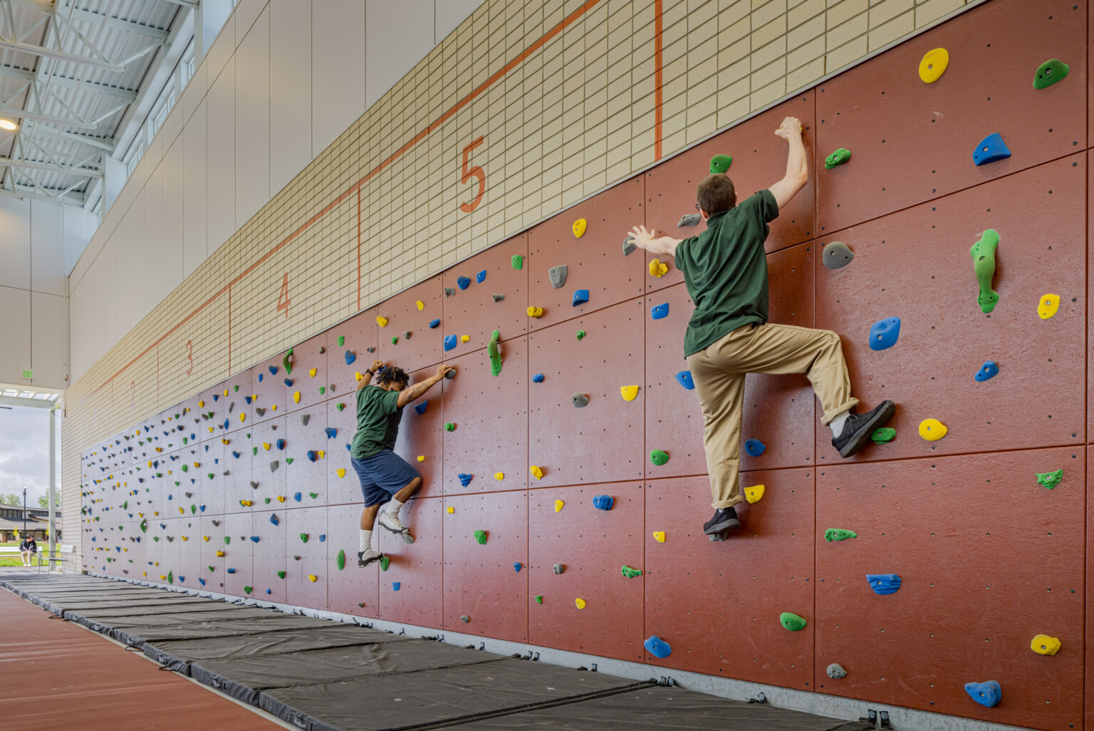 Two kids in green shirts climbing a rock wall with green, yellow, blue and grey rocks