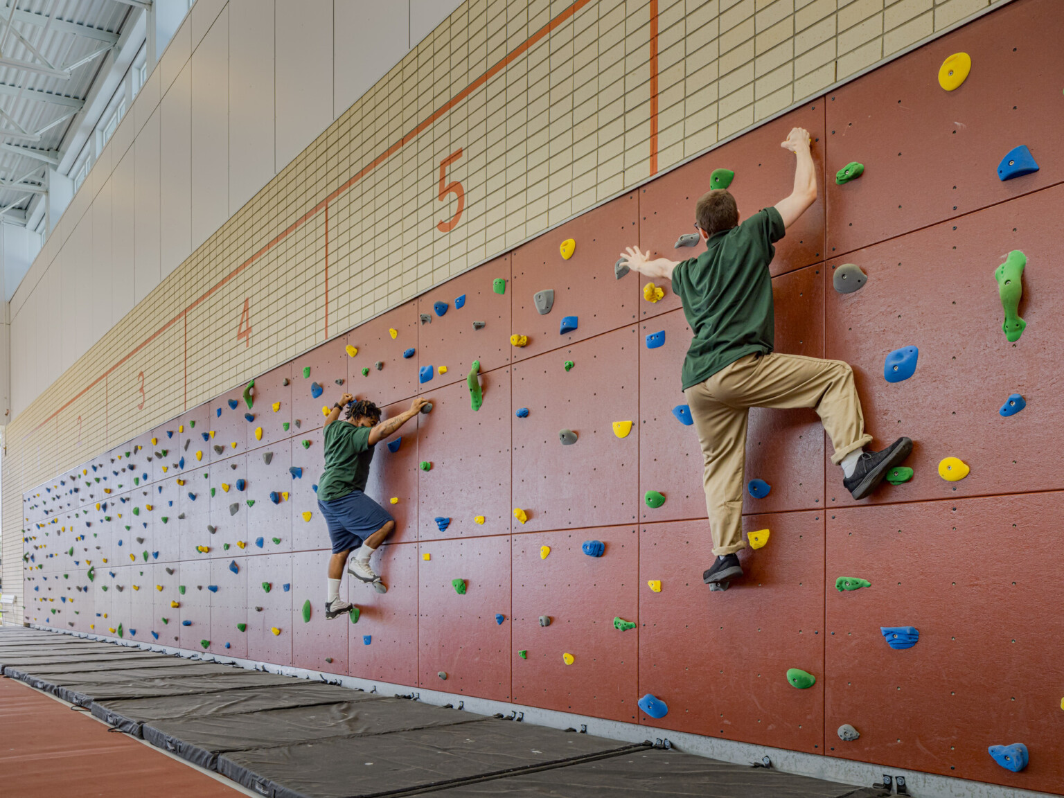 Two kids in green shirts climbing a rock wall with green, yellow, blue and grey rocks