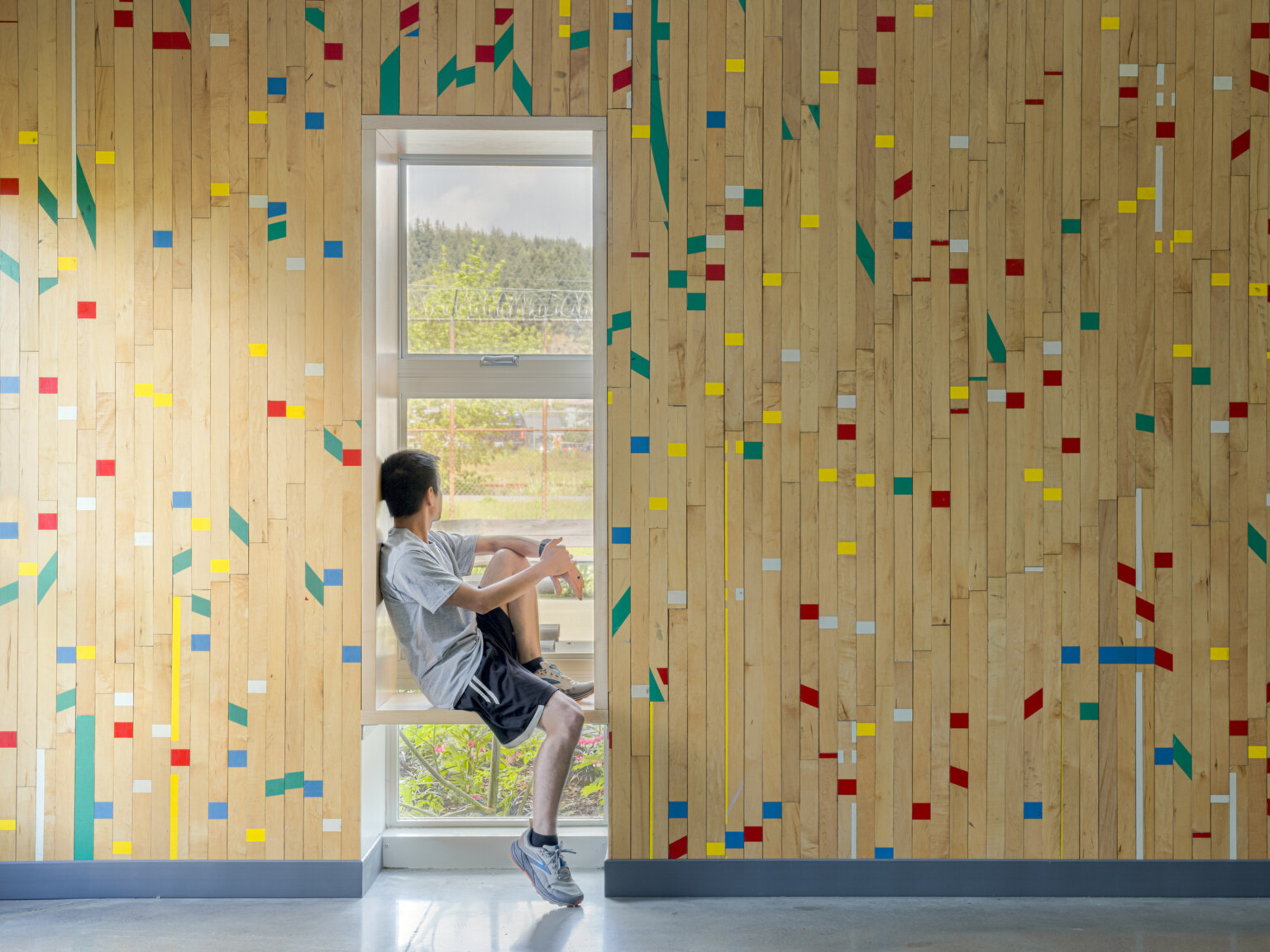 Wooden wall with green, blue, white, and yellow accent pieces with a young man sitting in a window seat