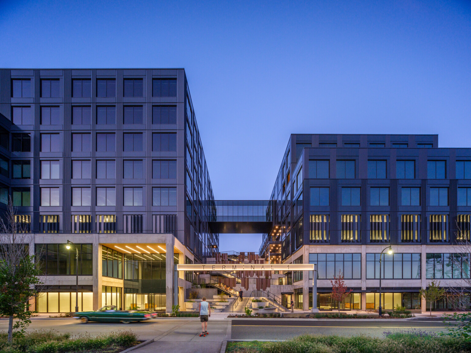 night view of multiple story mixd-use development, two large buildings connected by skyway, elevated bridgeway