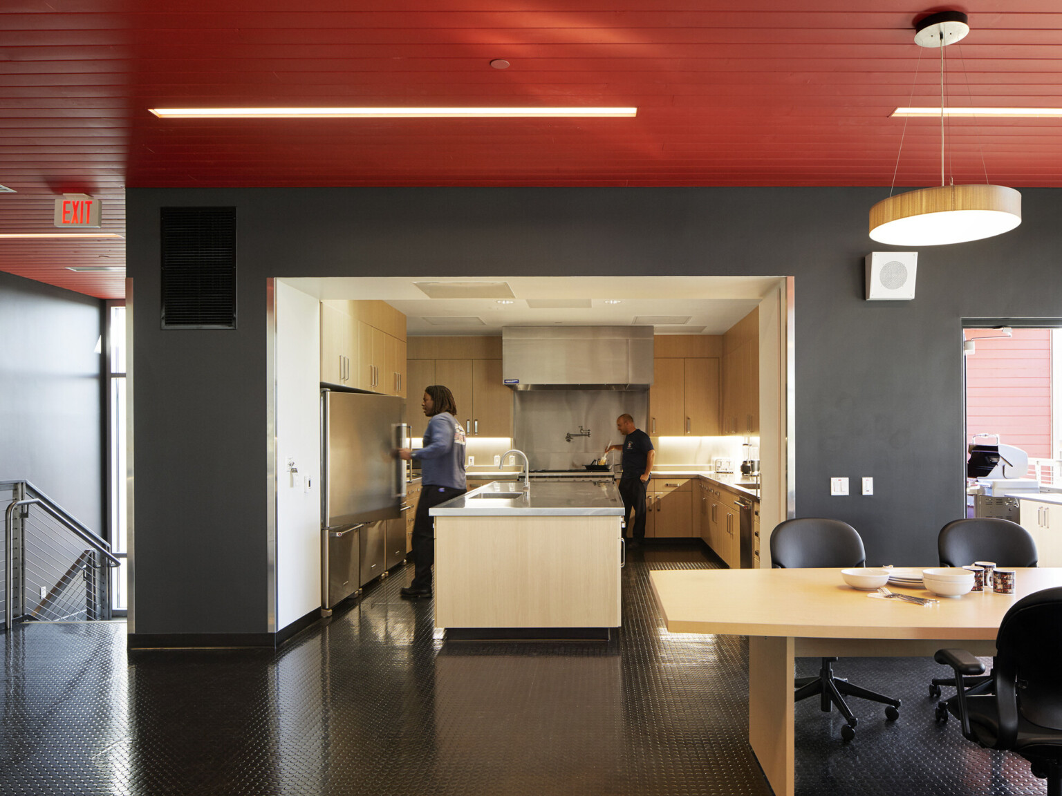 Kitchen of a fire station with black ceiling and floors with a red ceiling, natural wood cabinetry and furniture.