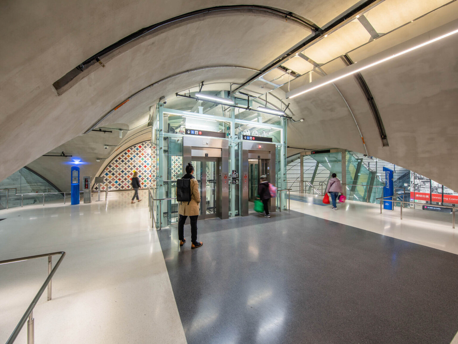 Domed upper level tunnel with stairs, back right, behind elevator shaft under construction. Raw concrete ceiling and floor