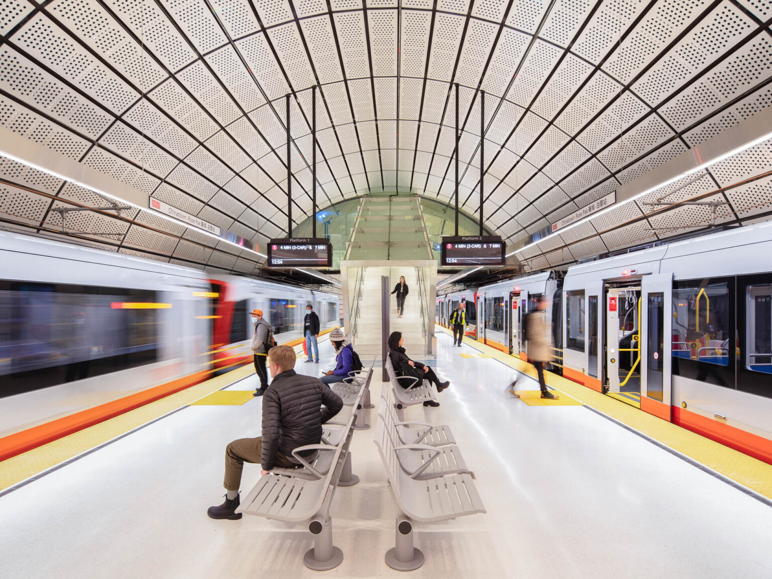 Rounded tunnel covered in perforated white panels. Hanging light beams along tracks beside screens