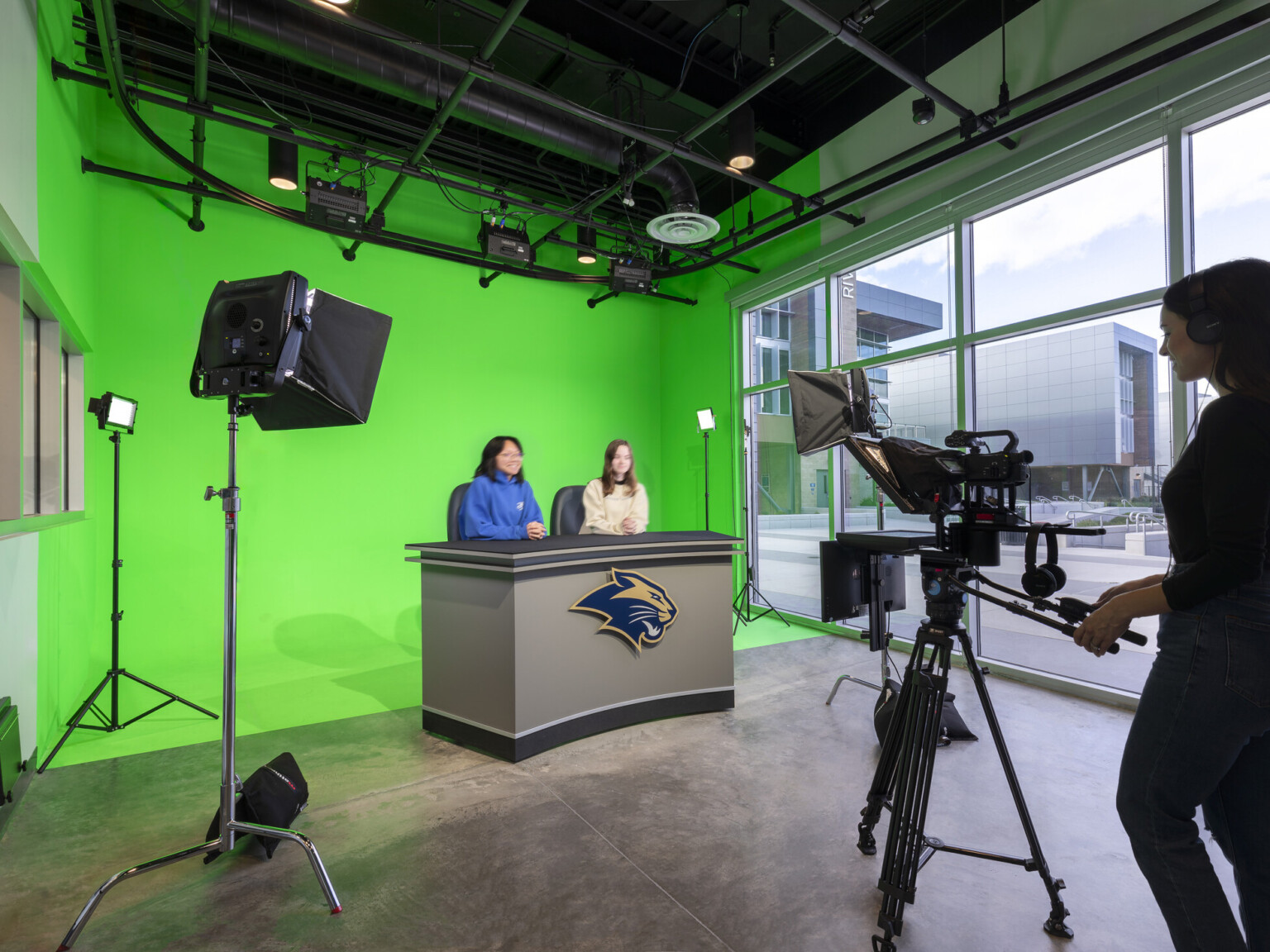 High school newsroom with two students sitting at a desk in front of a green wall