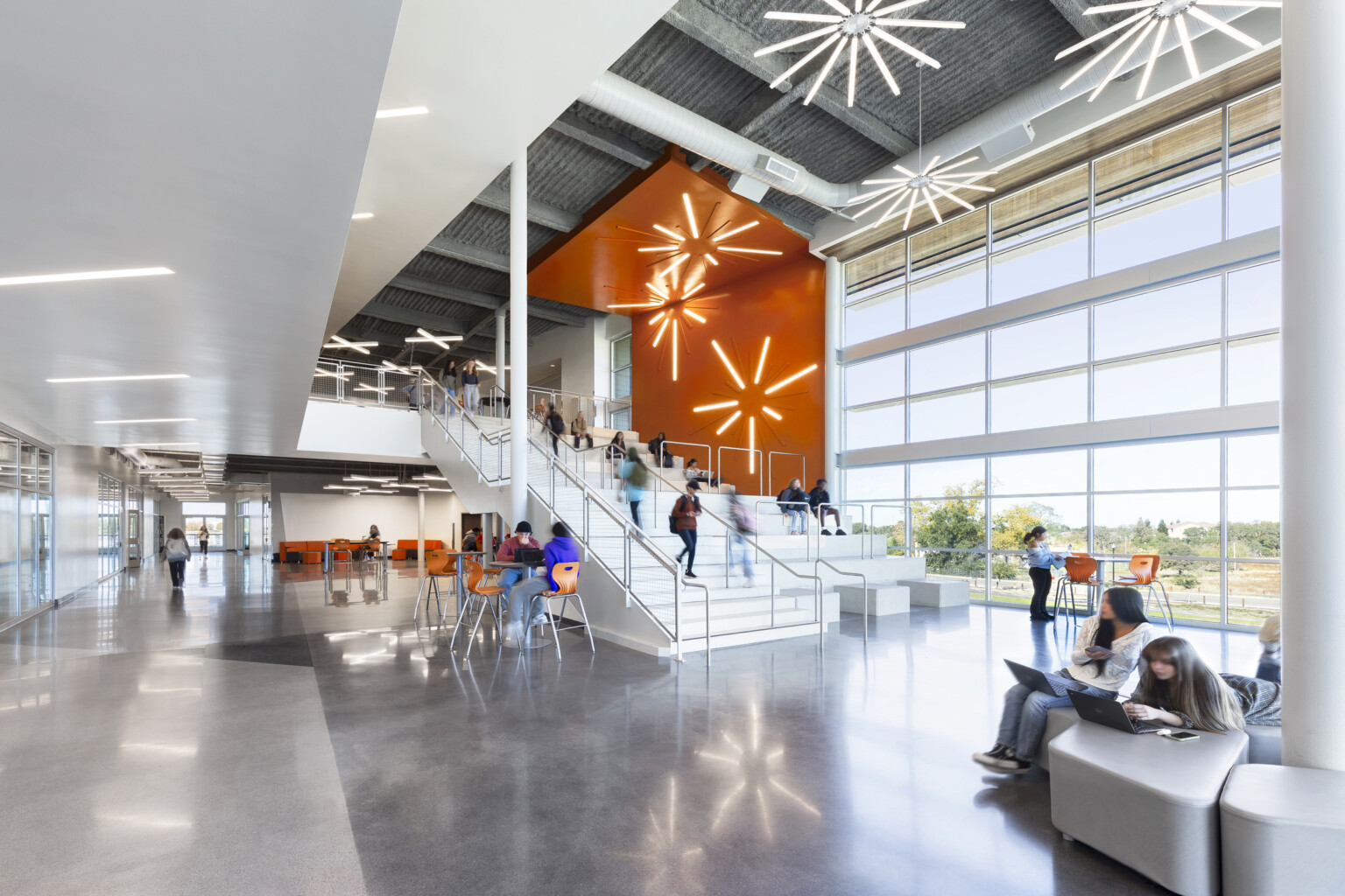 High school common area with modern lighting in star shapes suspended from the ceiling and on an orange accent wall over a staircase