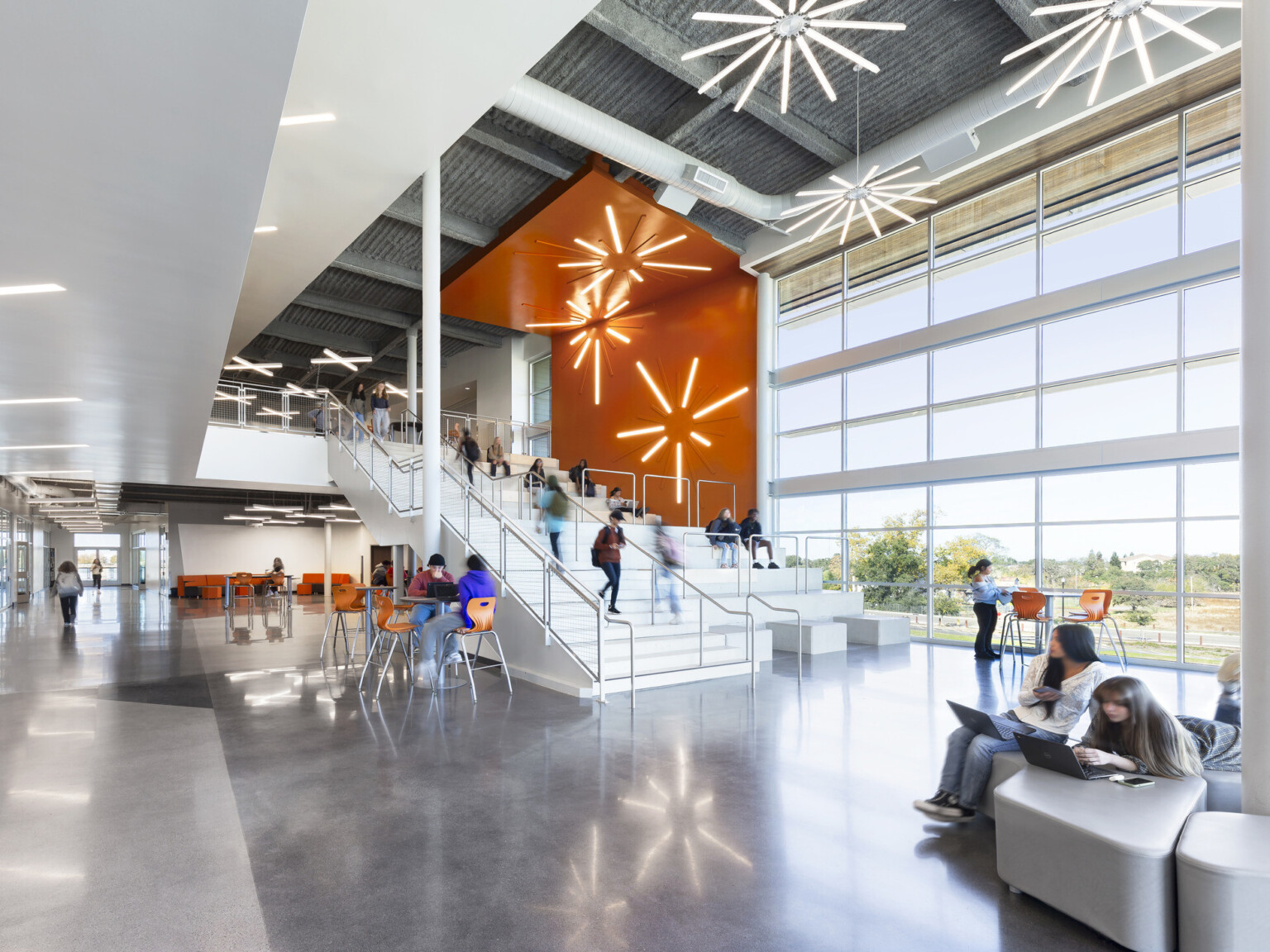 High school common area with modern lighting in star shapes suspended from the ceiling and on an orange accent wall over a staircase