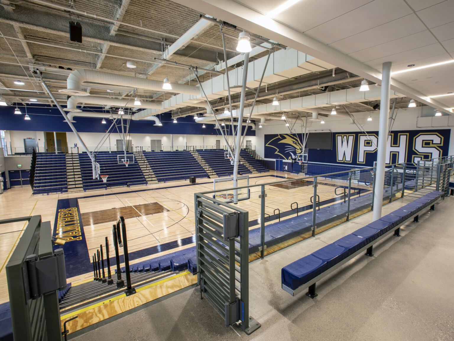 High school gym with blue seating areas with a blue accent wall with letters WPHS and basketball goals suspended from the ceiling