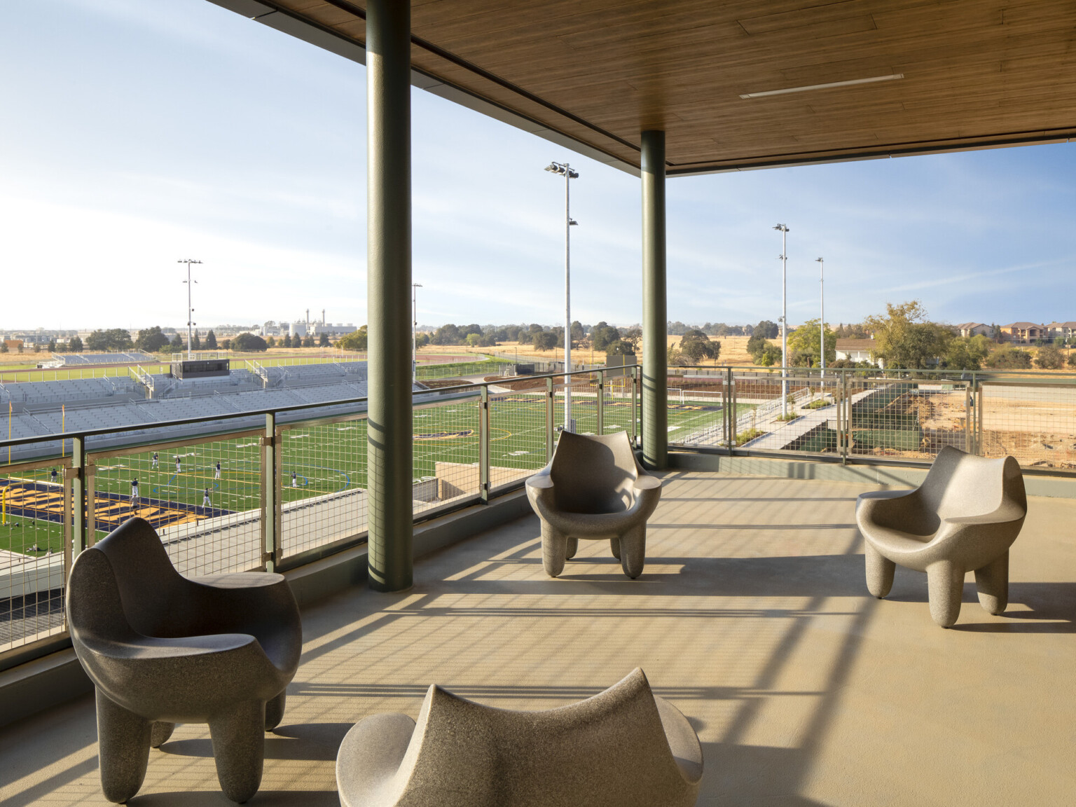 Balcony seating area with tan colored chairs overlooking a football field