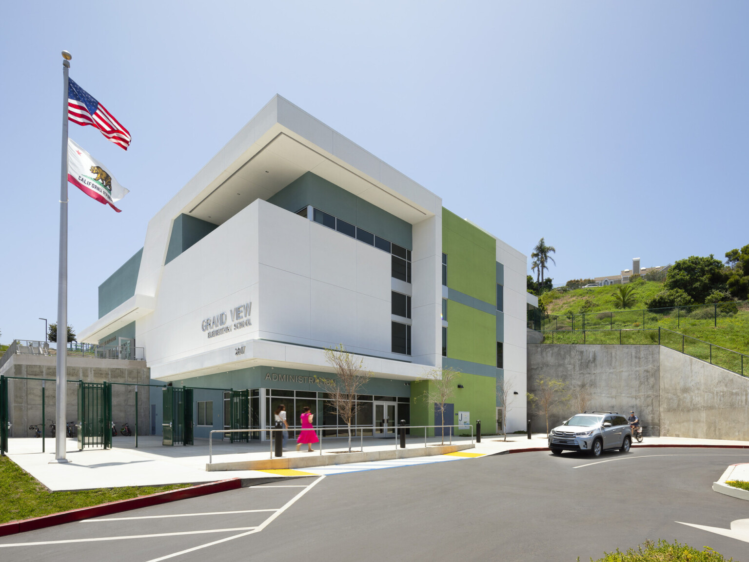 Rendering of a modern multistory building with green and blue accents, large hill with green grass in the back