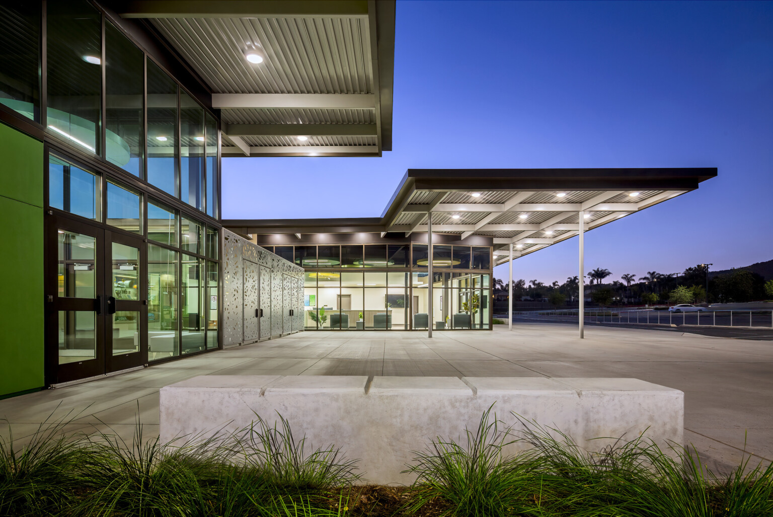 Canopy over building exterior entrance patio illuminated in the evening, large floor to ceiling windows