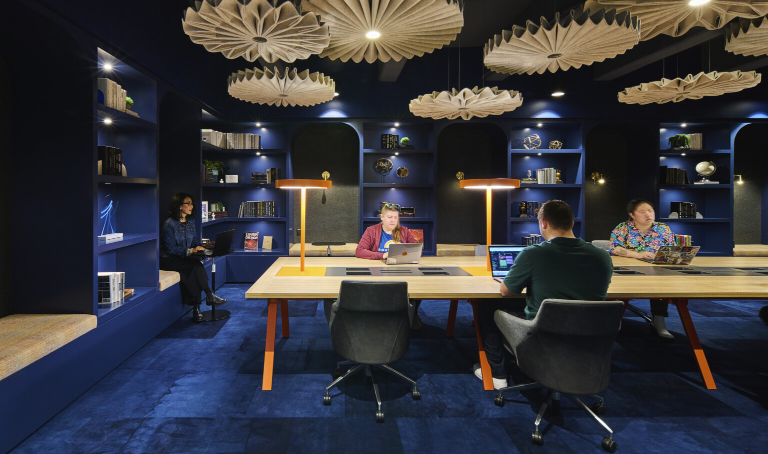 people working at a light wood table in a room with dark blue walls and ceilings, dark blue carpet and light wood chandeliers