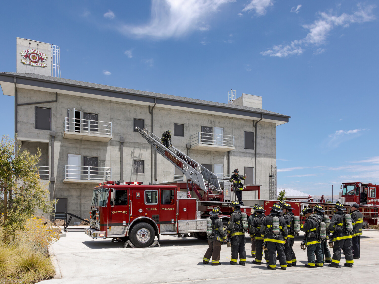 Firefighters dressed in safety gear standing in front of a fire truck with ladder extended to a concrete building