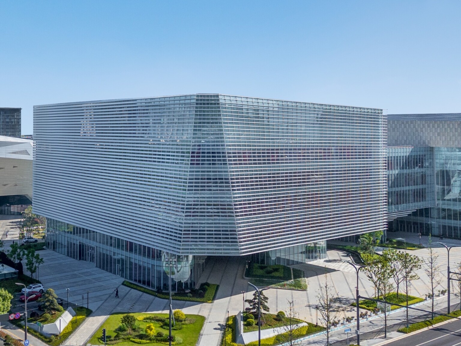 Modern multistory building filled with windows with metal accents. Lush Landscaping surrounded by concrete walkways