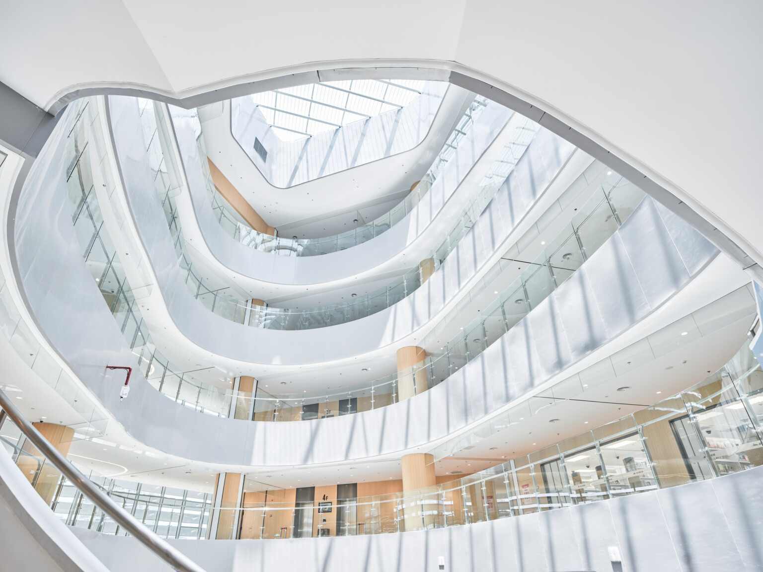 Modern building interior looking up multiple stories at glass railings, white walls, and natural wood accents