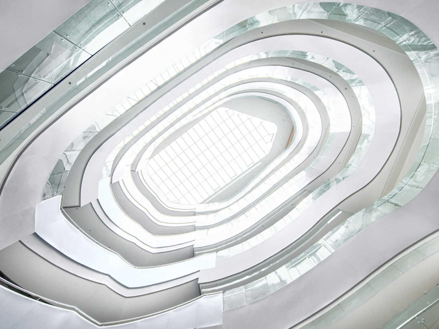 Modern stairway looking up at a glass ceiling and multiple levels of glass railings with white accents